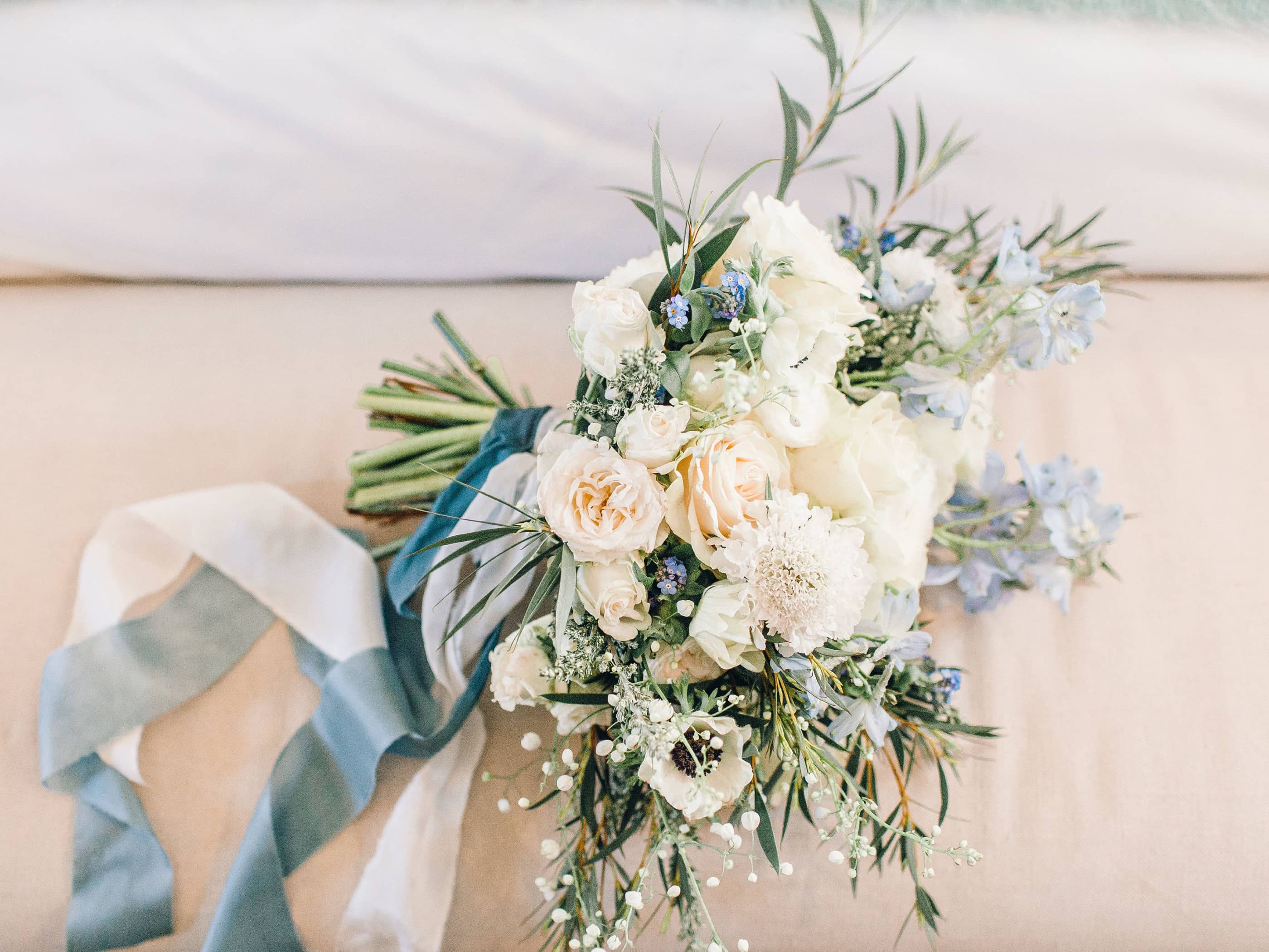 A bridal bouquet containing white and blue flowers, tied with a blue velvet and chiffon ribbon.