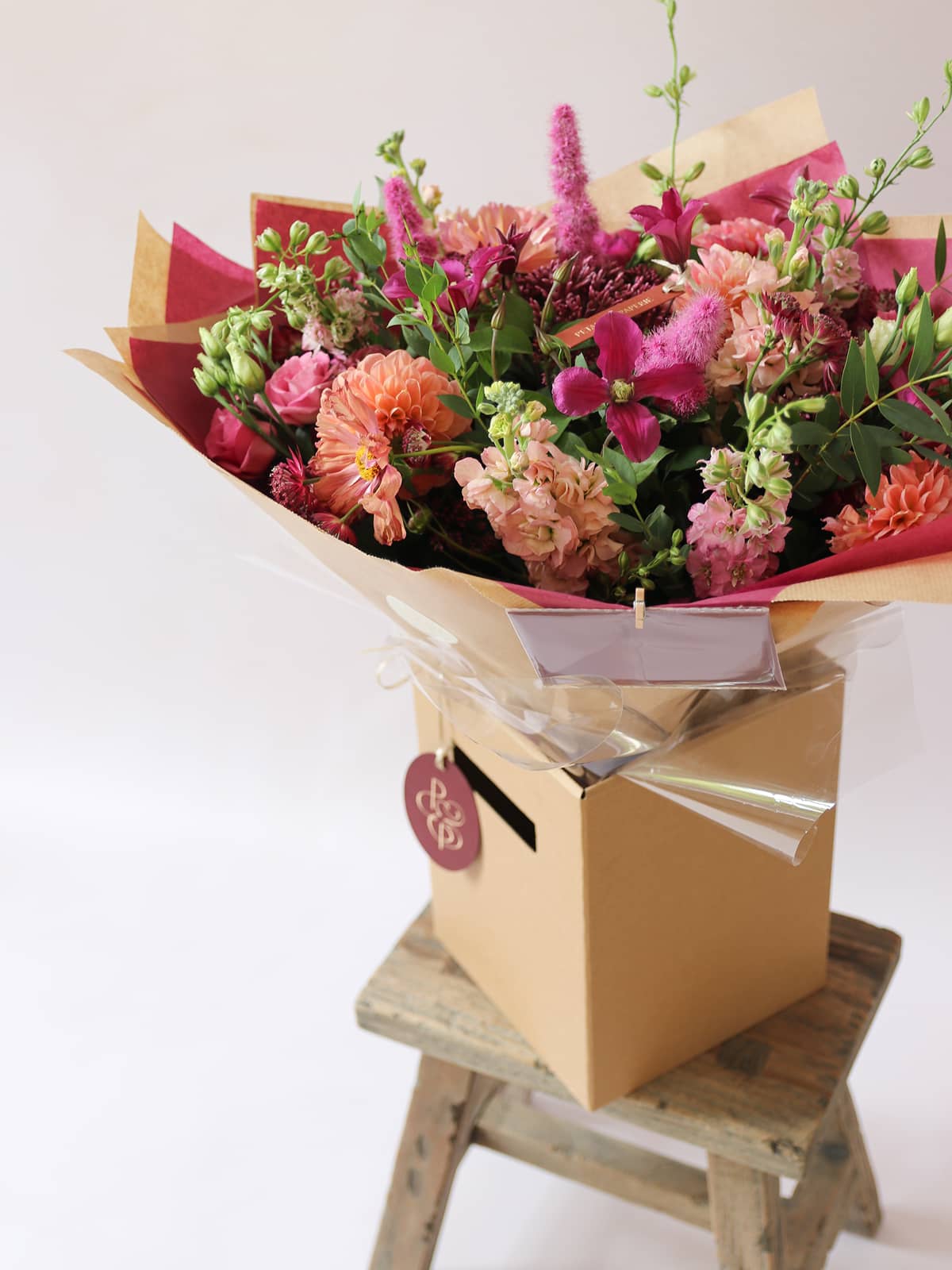 Bouquet of flowers in a cardboard box on a wooden stool with a white background