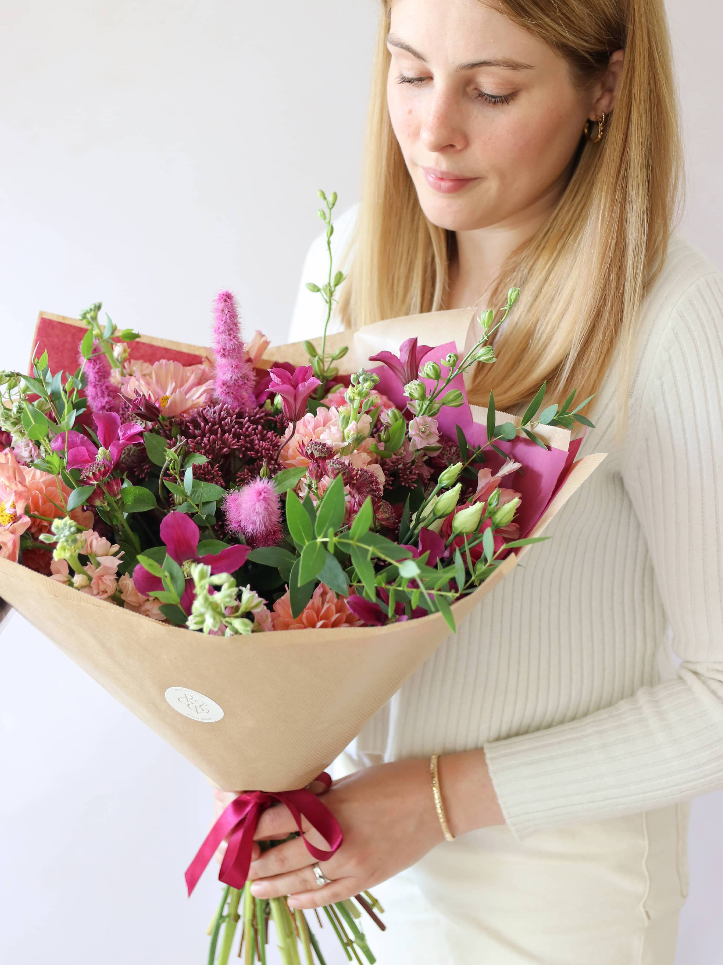 Woman holding a bouquet of bright pink and peach flowers against a white background