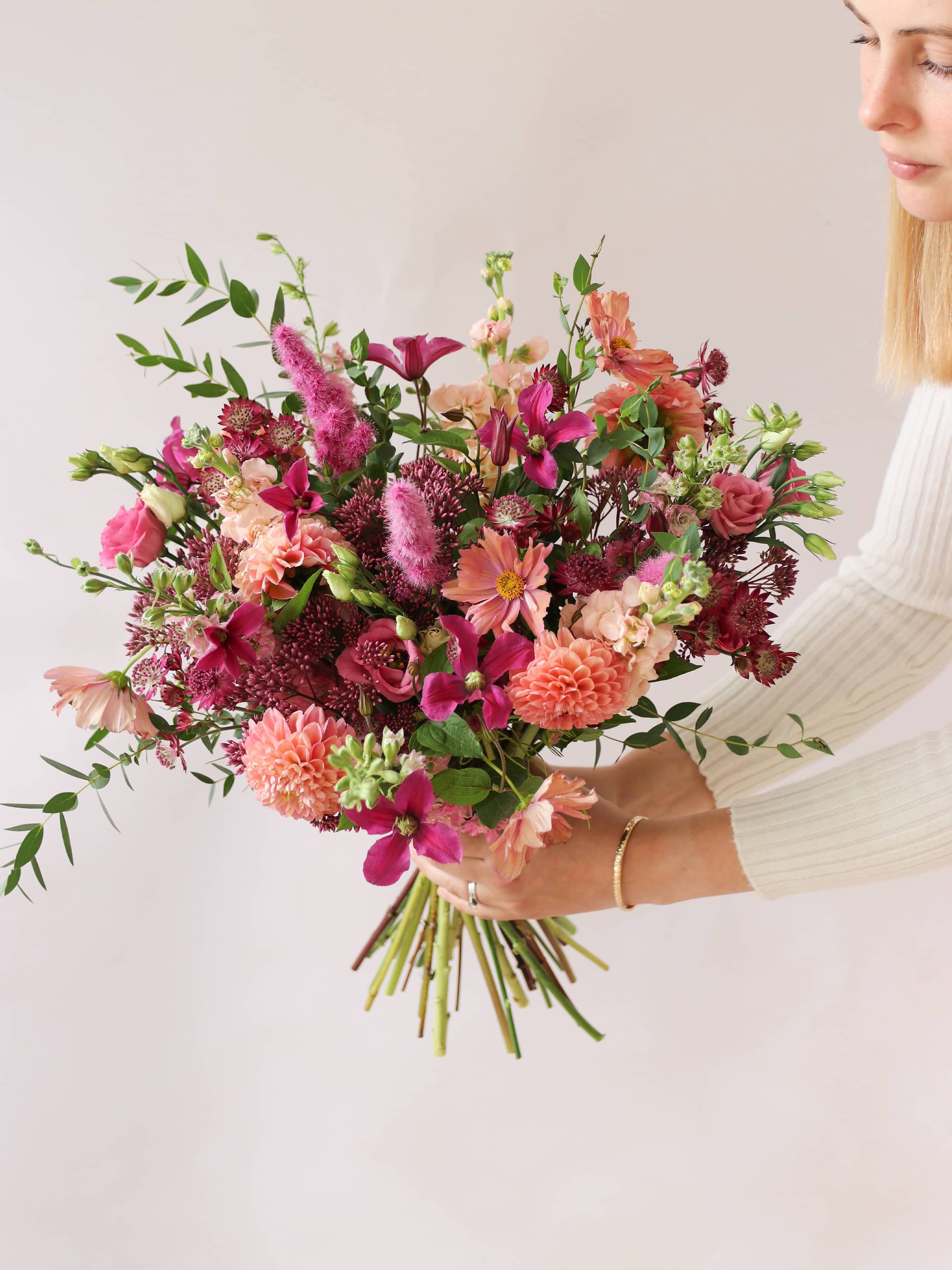 Bouquet of bright pink and peach flowers held by a person against a neutral background