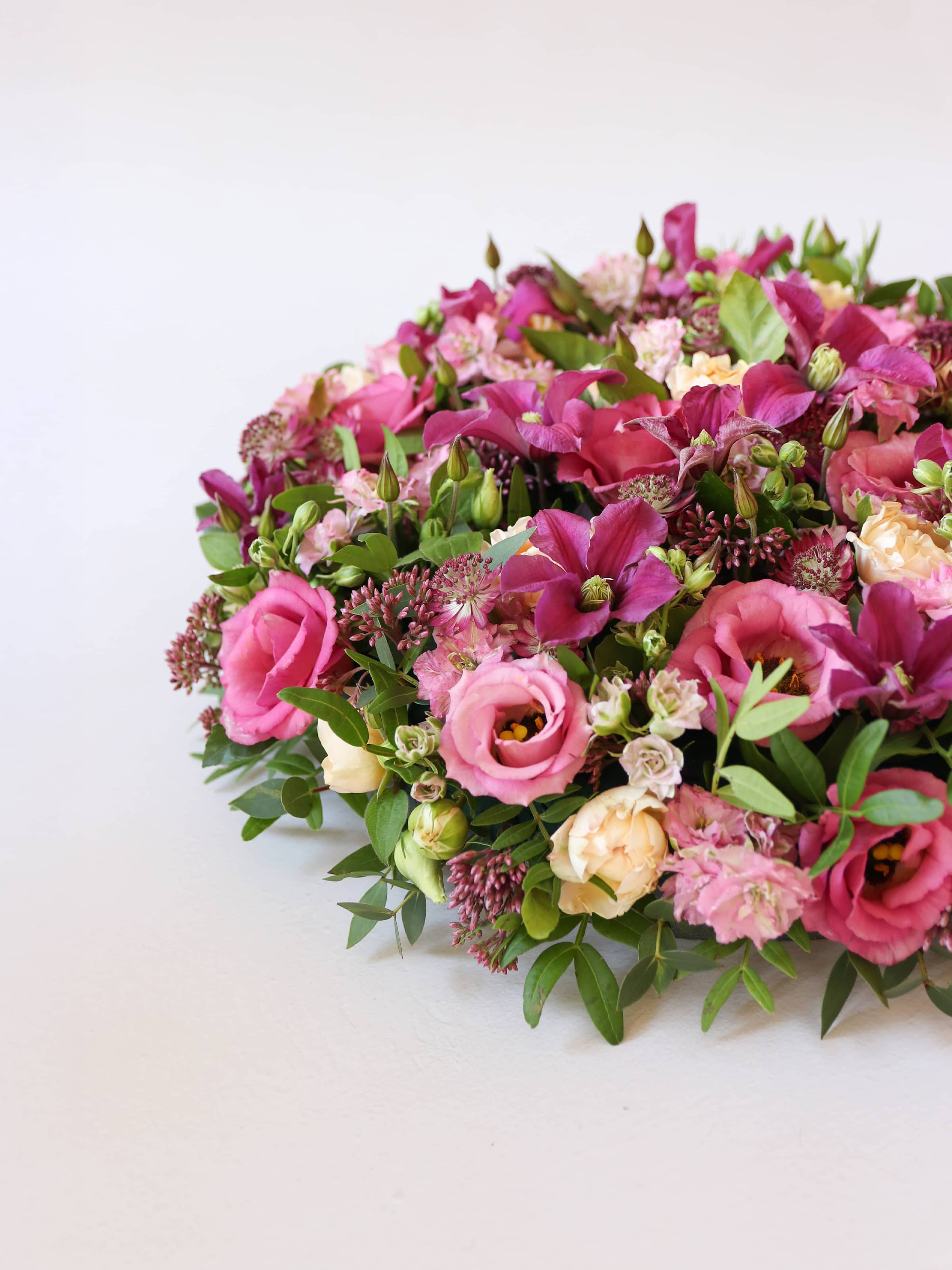 Off canvas view of a round funeral posy of bright pink and peach flowers with green foliage on a white background