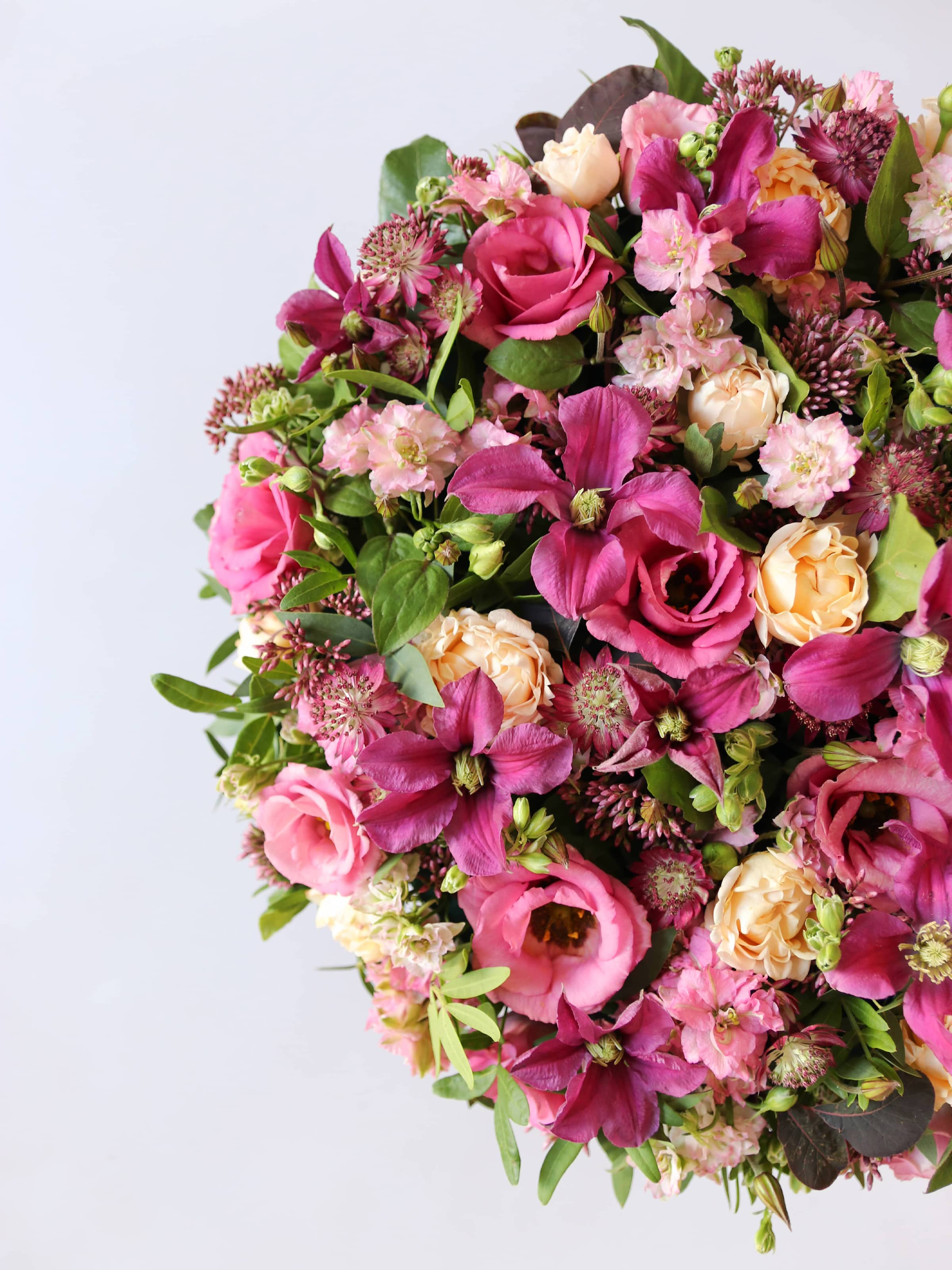 Top down, off canvas view of a round funeral posy of bright pink and peach flowers with green foliage on a white background