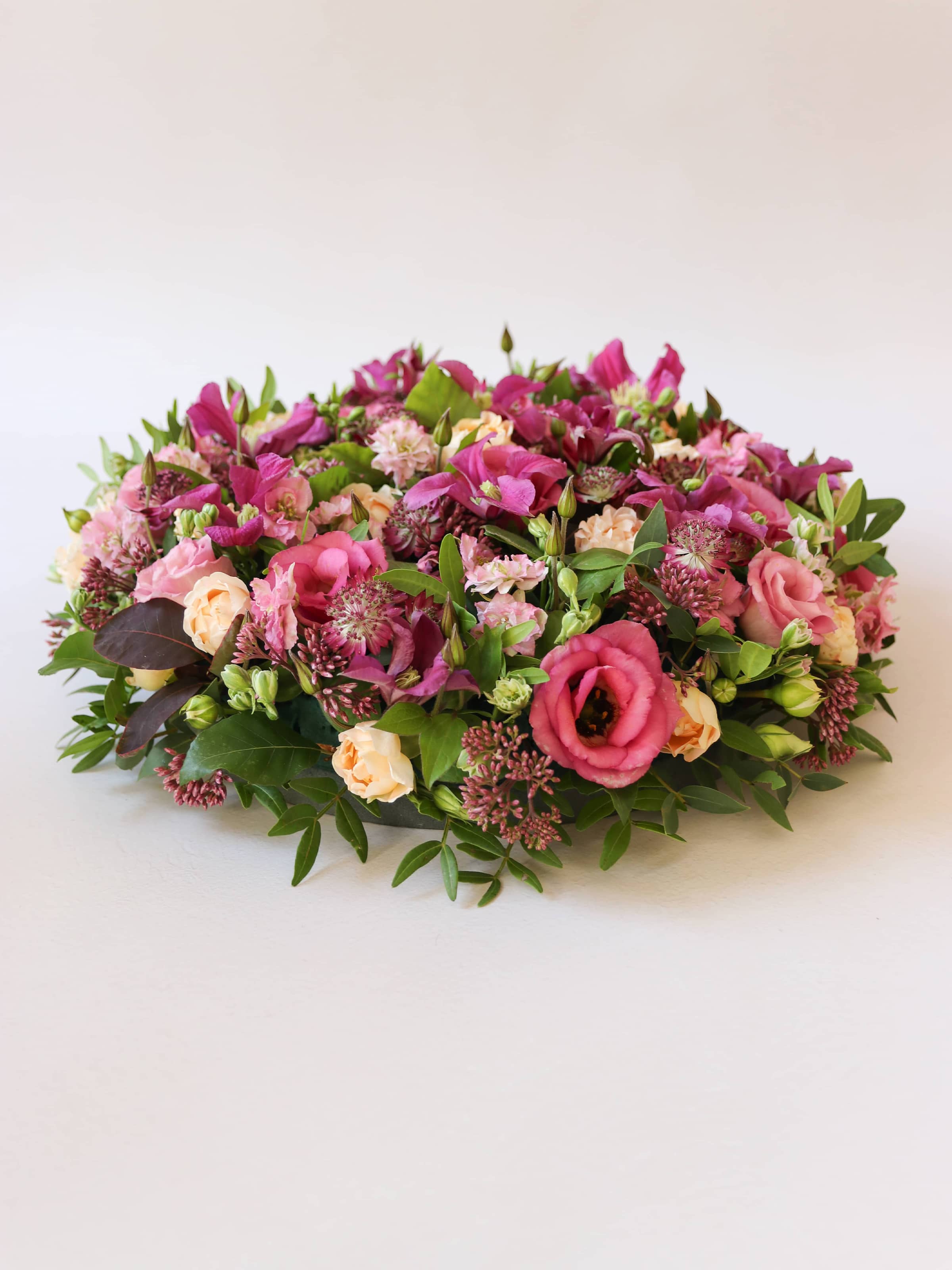 Side view of a round funeral posy of bright pink and peach flowers with green foliage on a white background