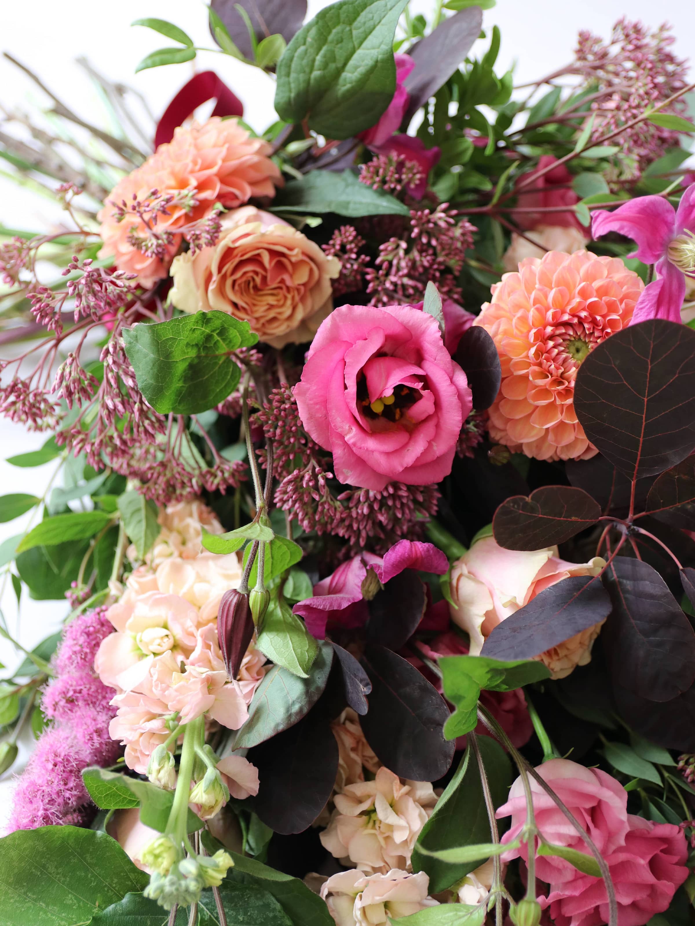 Colourful, top down view of a funeral sheaf with pink, orange, and purple tones on a neutral background.