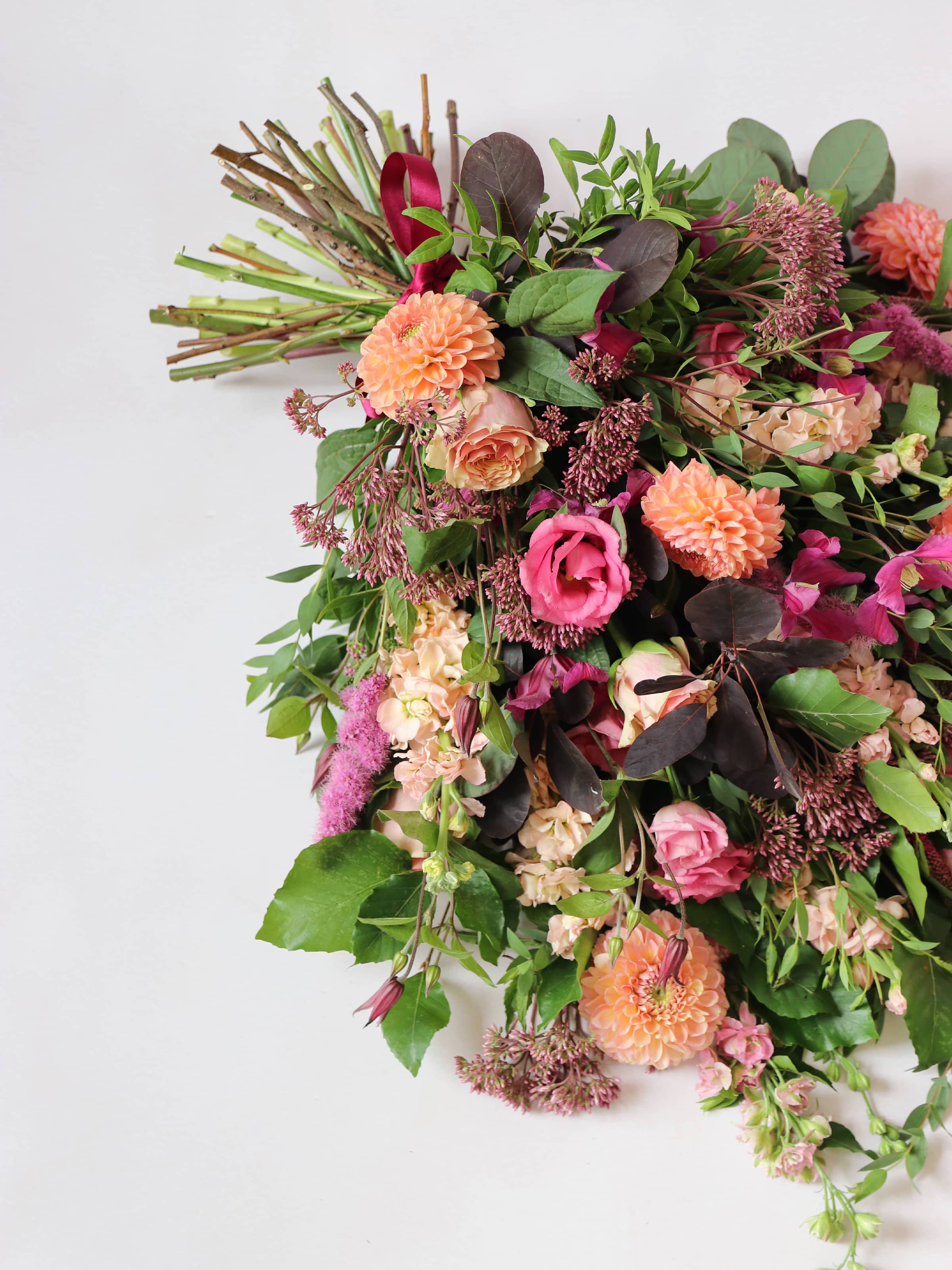 Top down view of a funeral sheaf with bright pink and peach flowers with green foliage on a white background.
