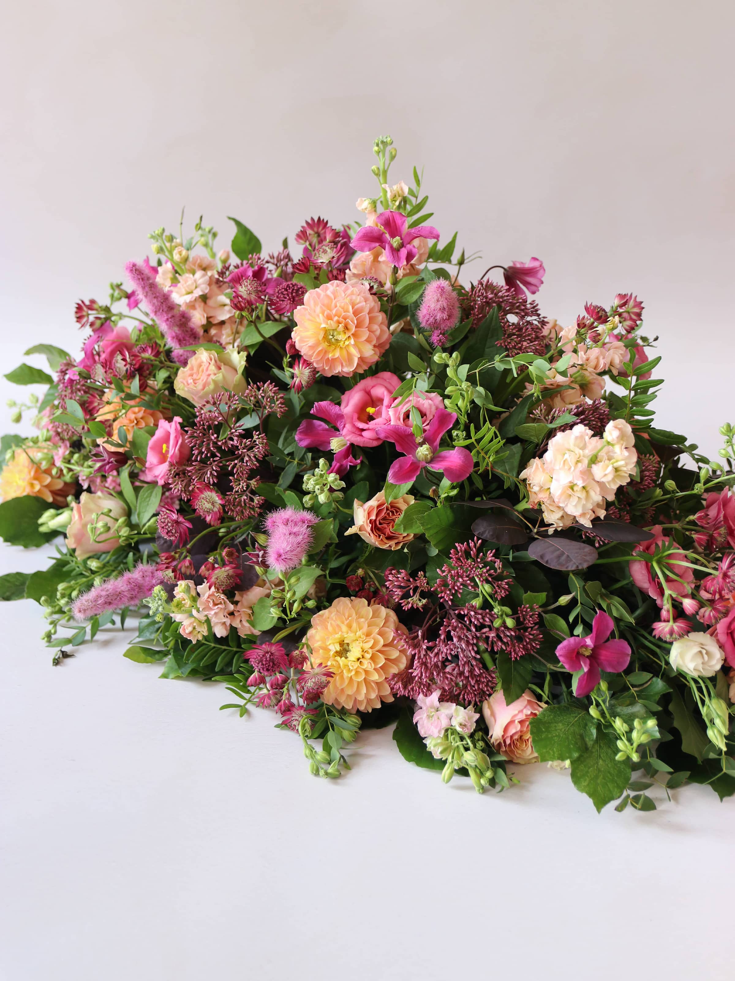 Bright pink and peach coffin spray with green foliage at an angle on a white background
