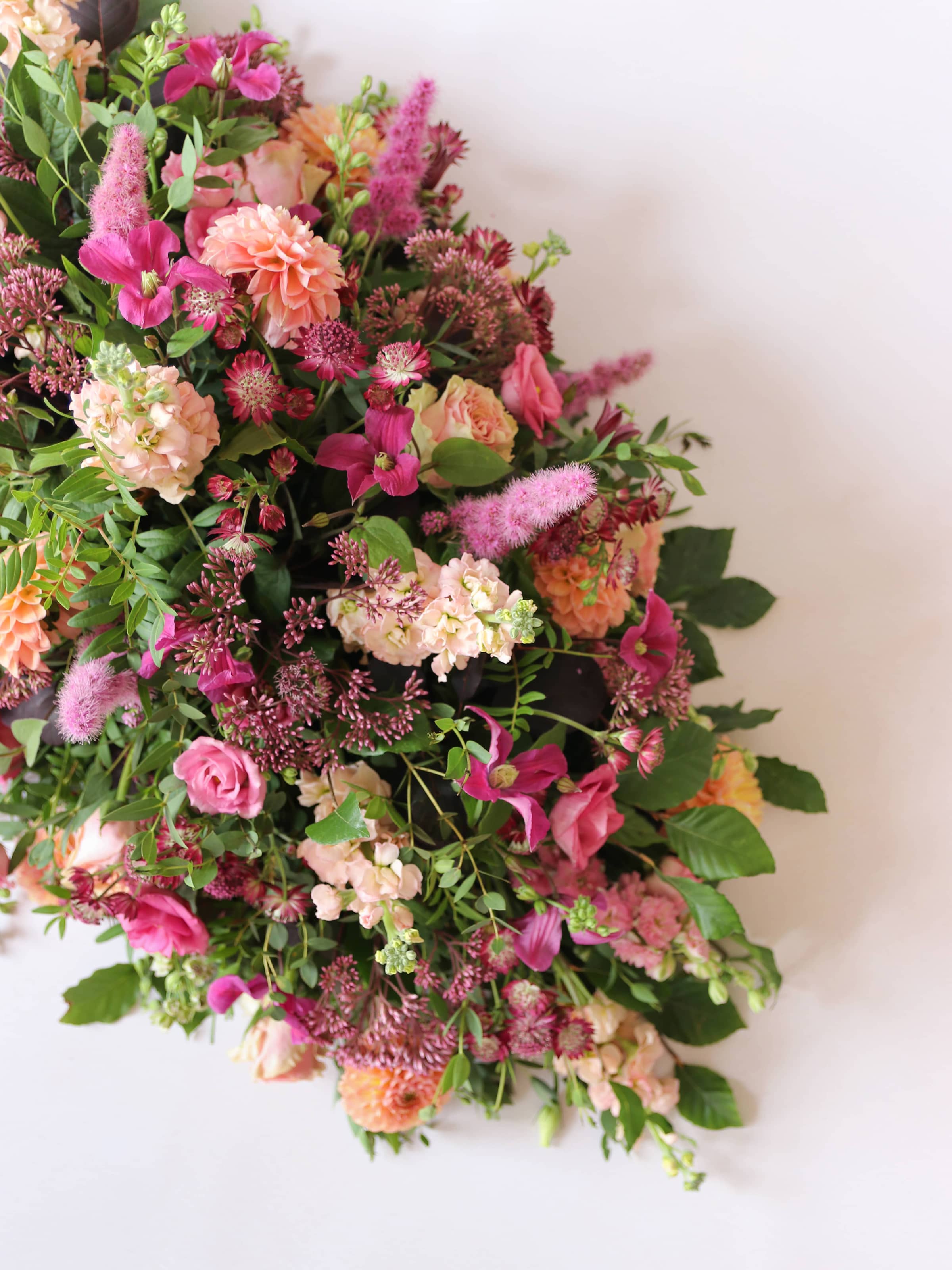 One end of a double ended coffin spray with bright pink and peach flowers, on a white background