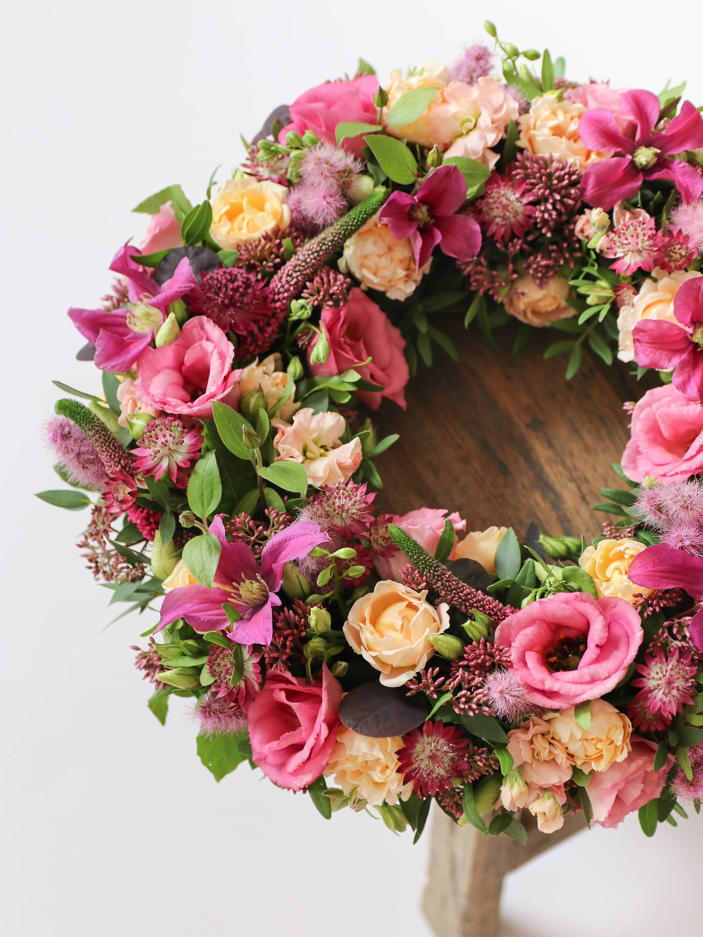 Floral wreath with pink, yellow, and green flowers on a wooden stool
