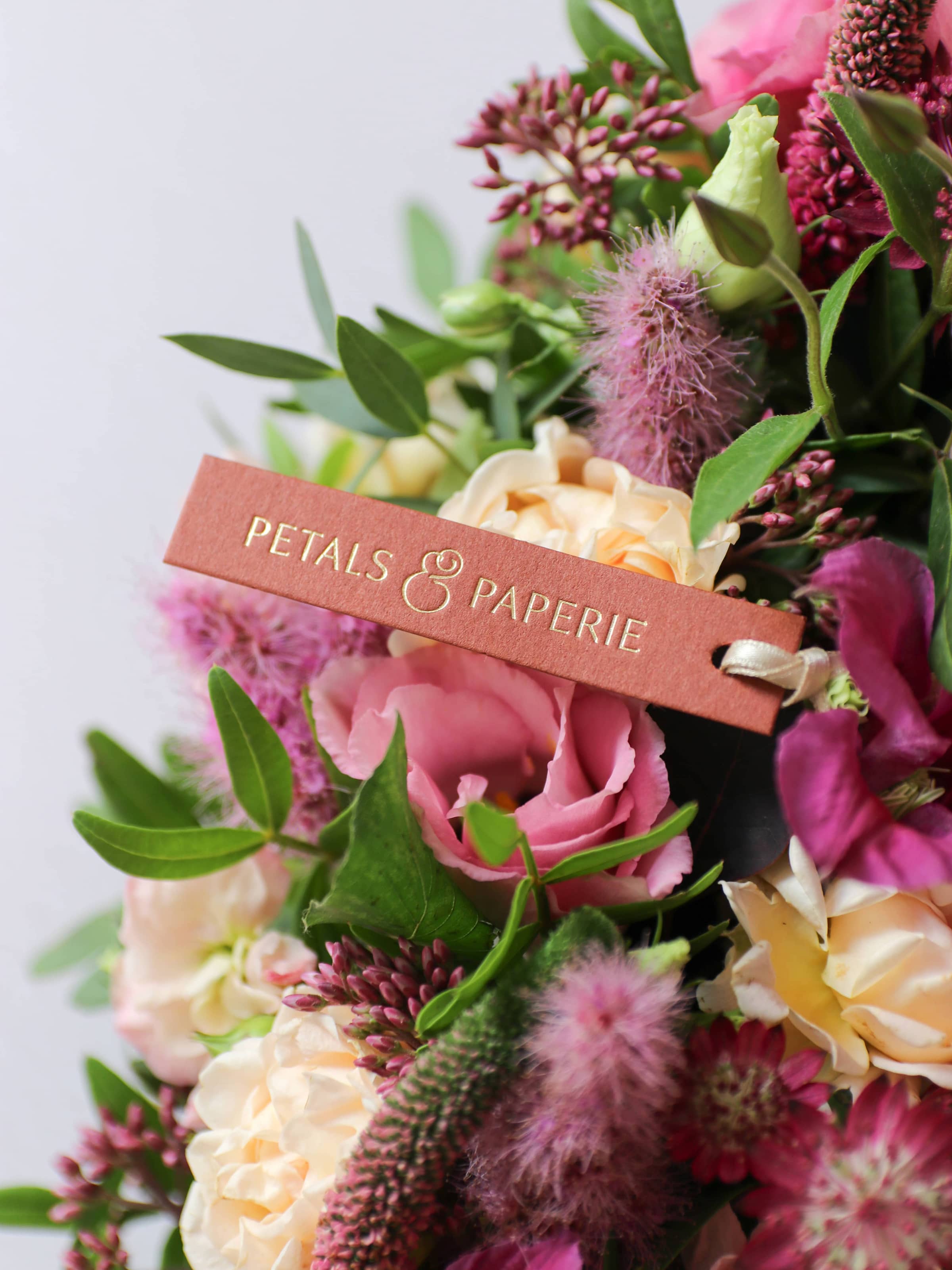 Bouquet of bright pinks and green flowers with a 'Petals & Paperie' tag