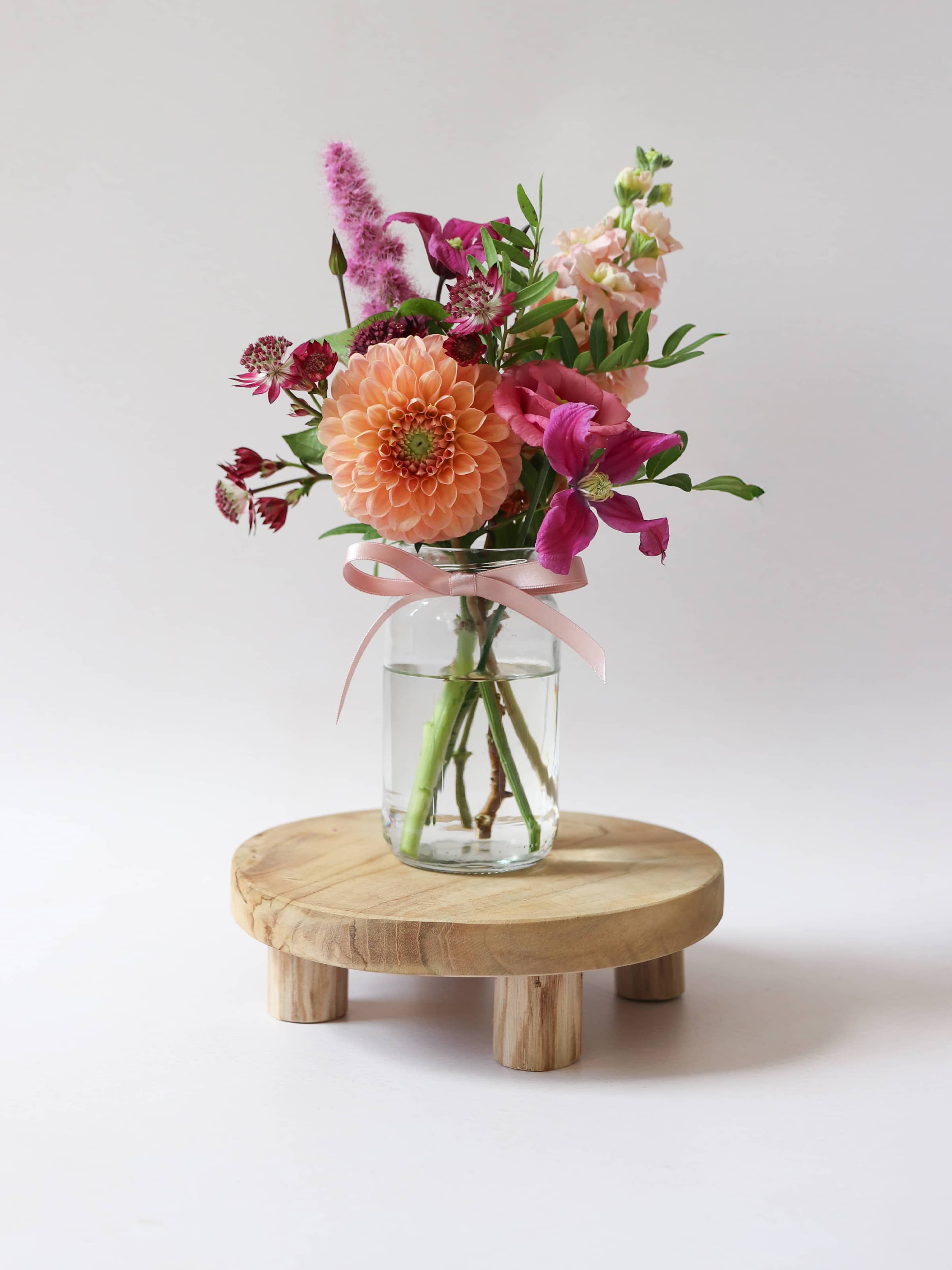 Glass vase with bright pink and peach on a wooden stand against a white background