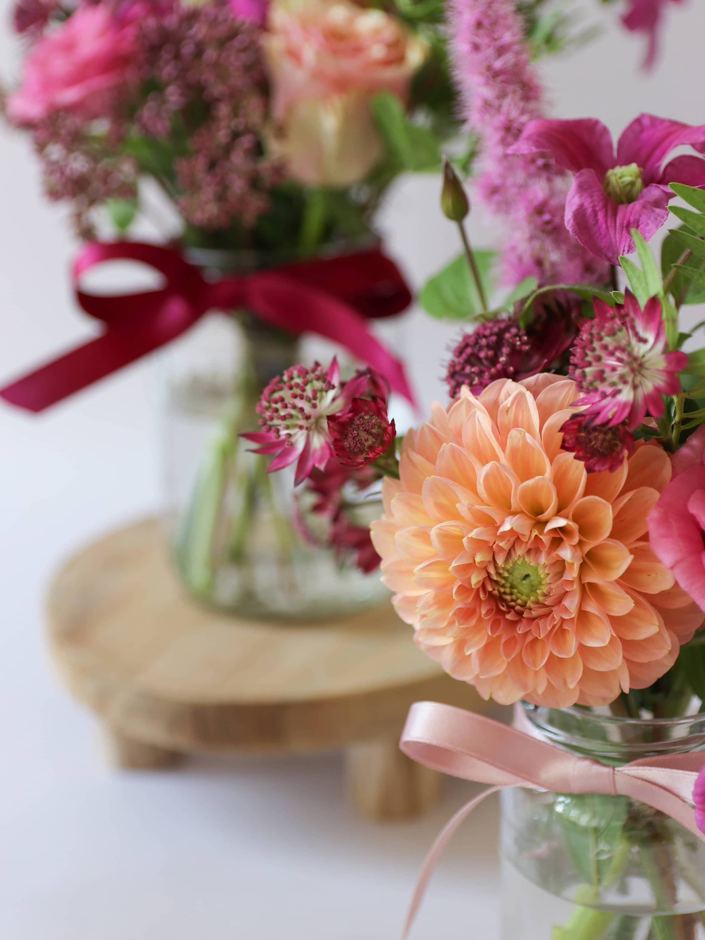 Trio of bright pink and peach flower arrangements in glass jam jars with ribbons on a white background