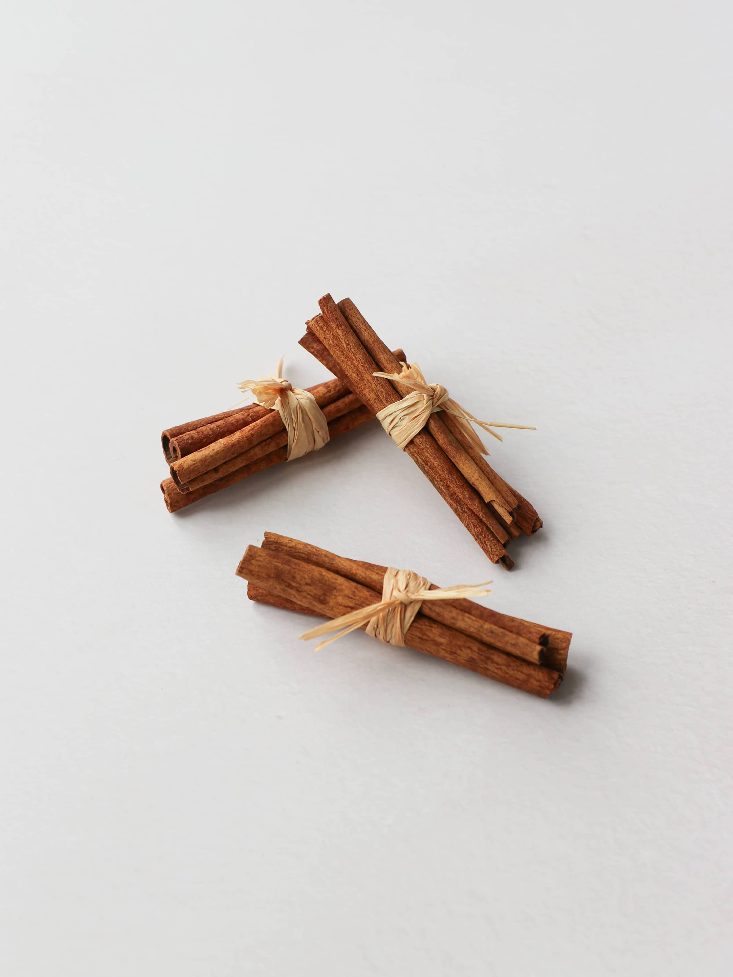 Three bundles of cinnamon sticks tied with raffia for Christmas wreath making, on a neutral background.