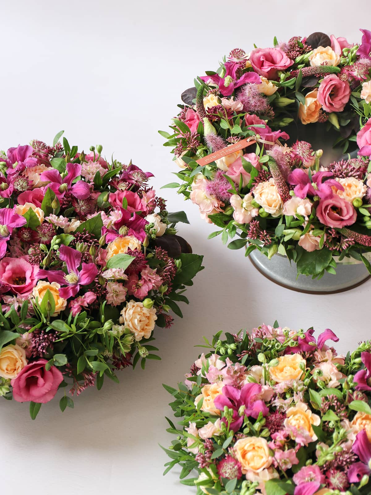 Three floral funeral posy's with pink, yellow, and green flowers on a white background