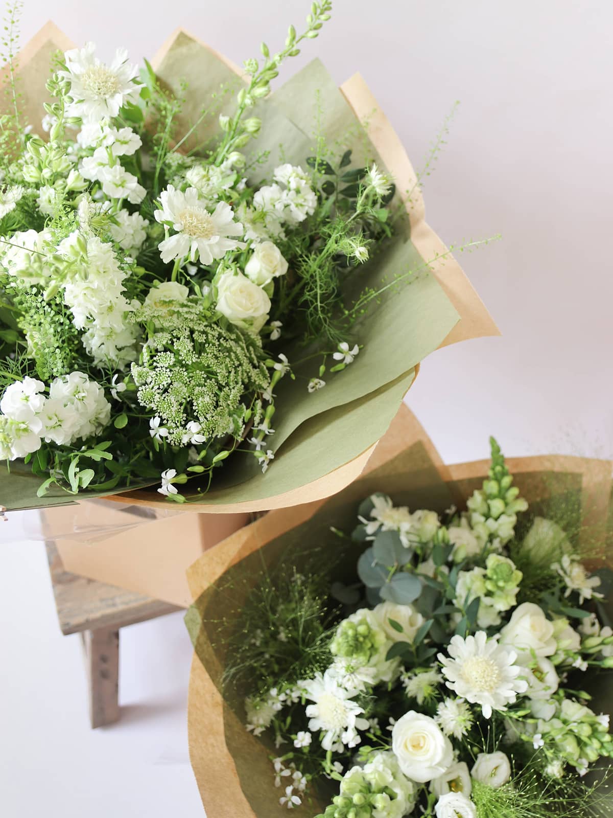 Two bouquets of white and green flowers wrapped in brown craft paper on a white background
