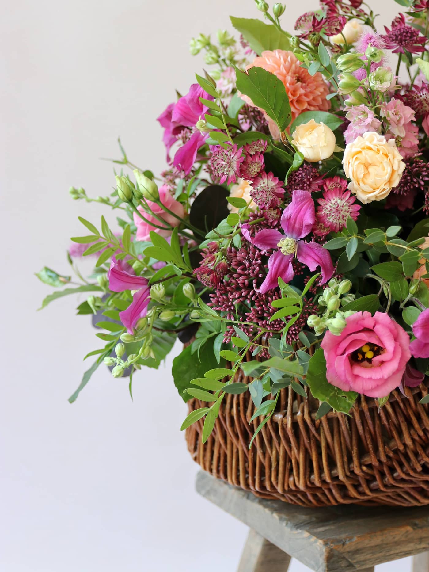 An arrangement of colourful pink, peach and purple flowers in a wicker basket on a neutral background