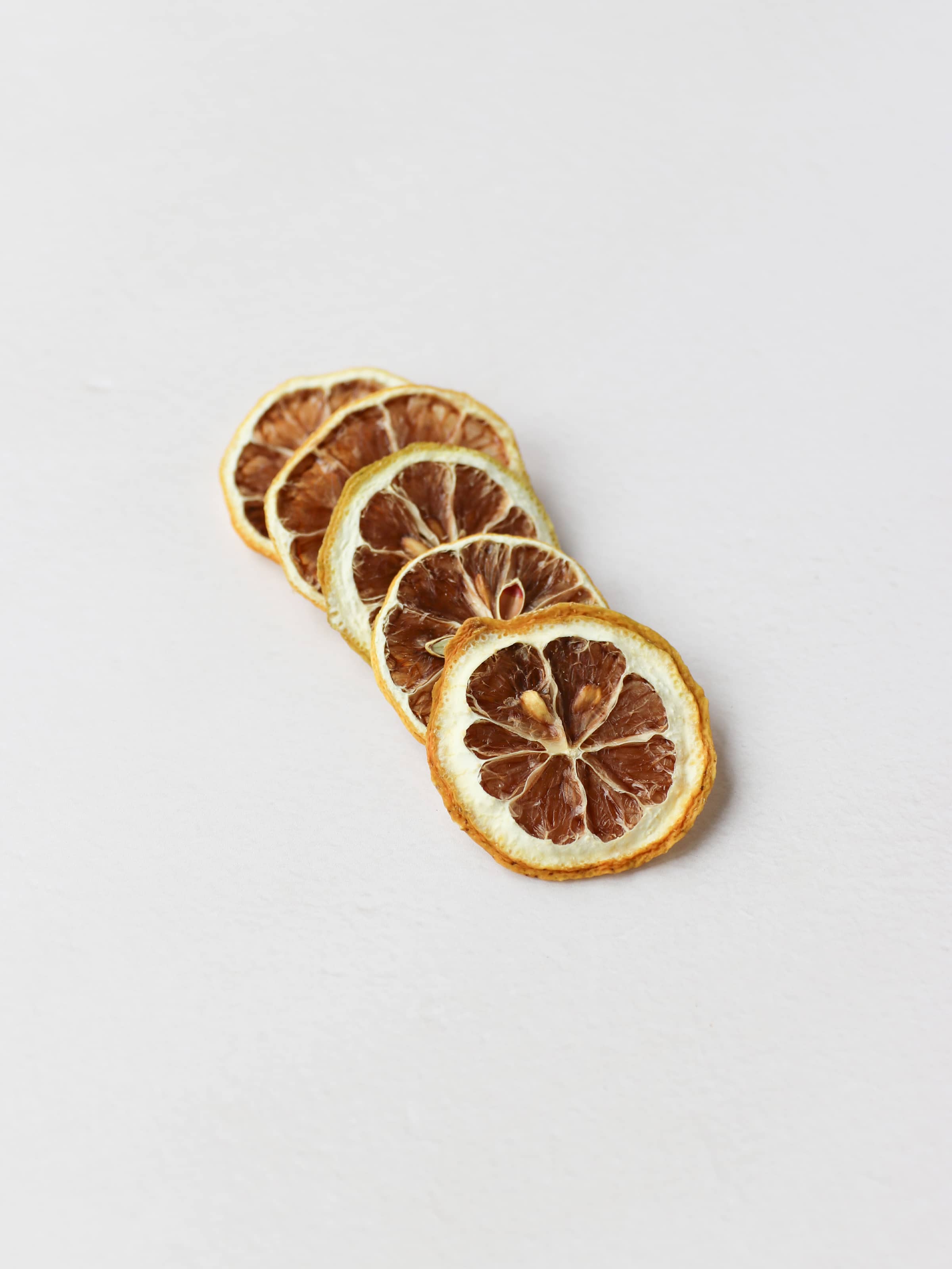 A top view of 5 dried lemon slices positioned in a diagonal row on a light neutral background.