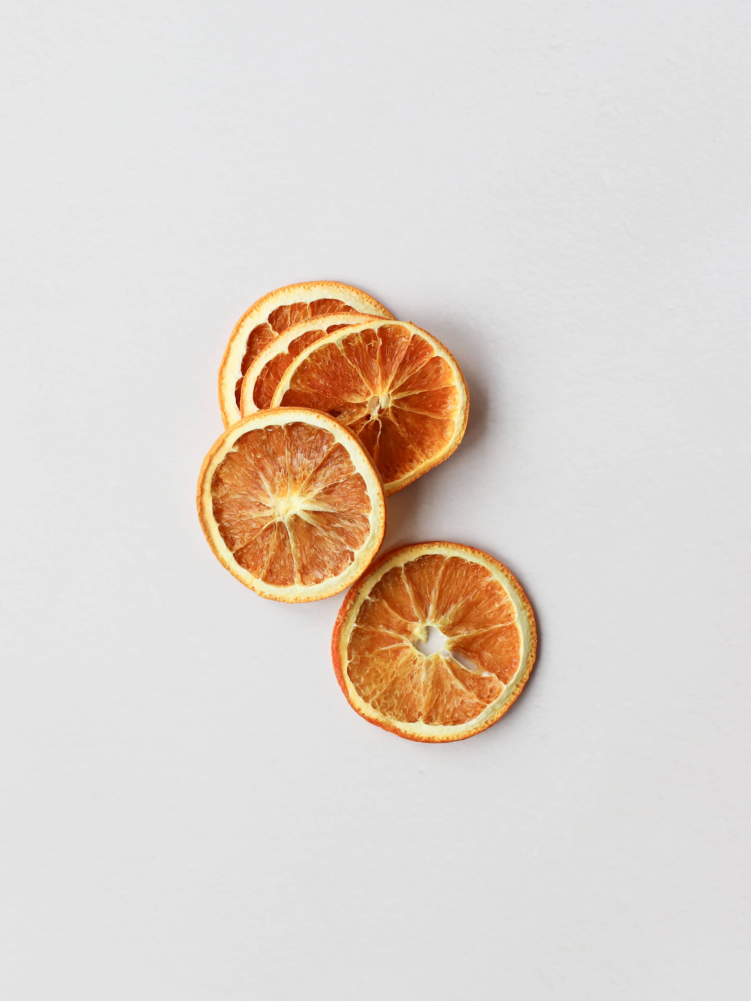 Five dried orange slices for Christmas wreath making, lying in a vertical row on a light background.