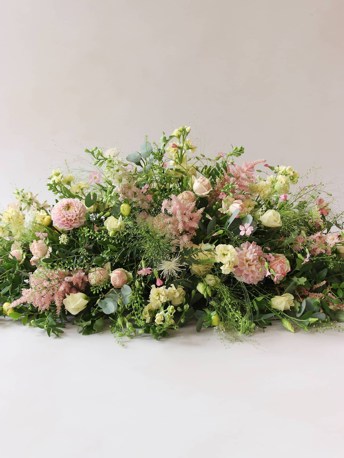 Double ended coffin spray with pastel flowers and greenery on a white surface