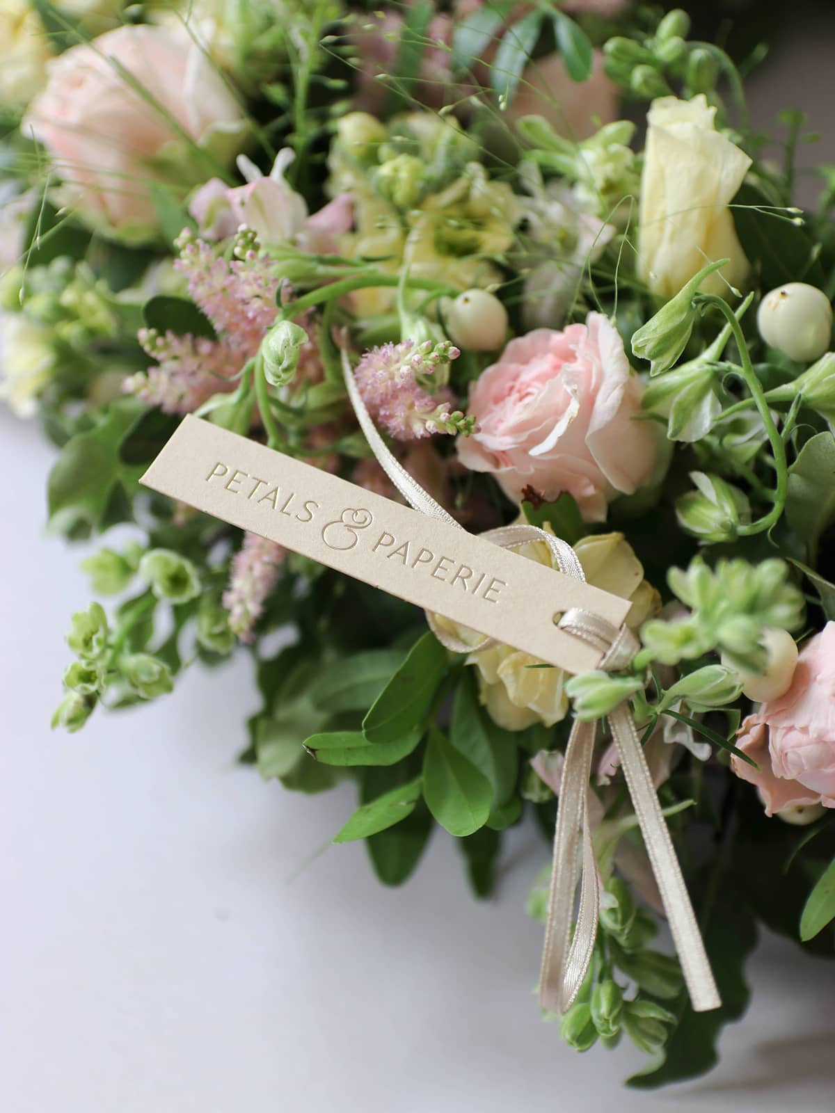 Bouquet of pastel flowers with a 'Petals & Paperie' tag on a white background