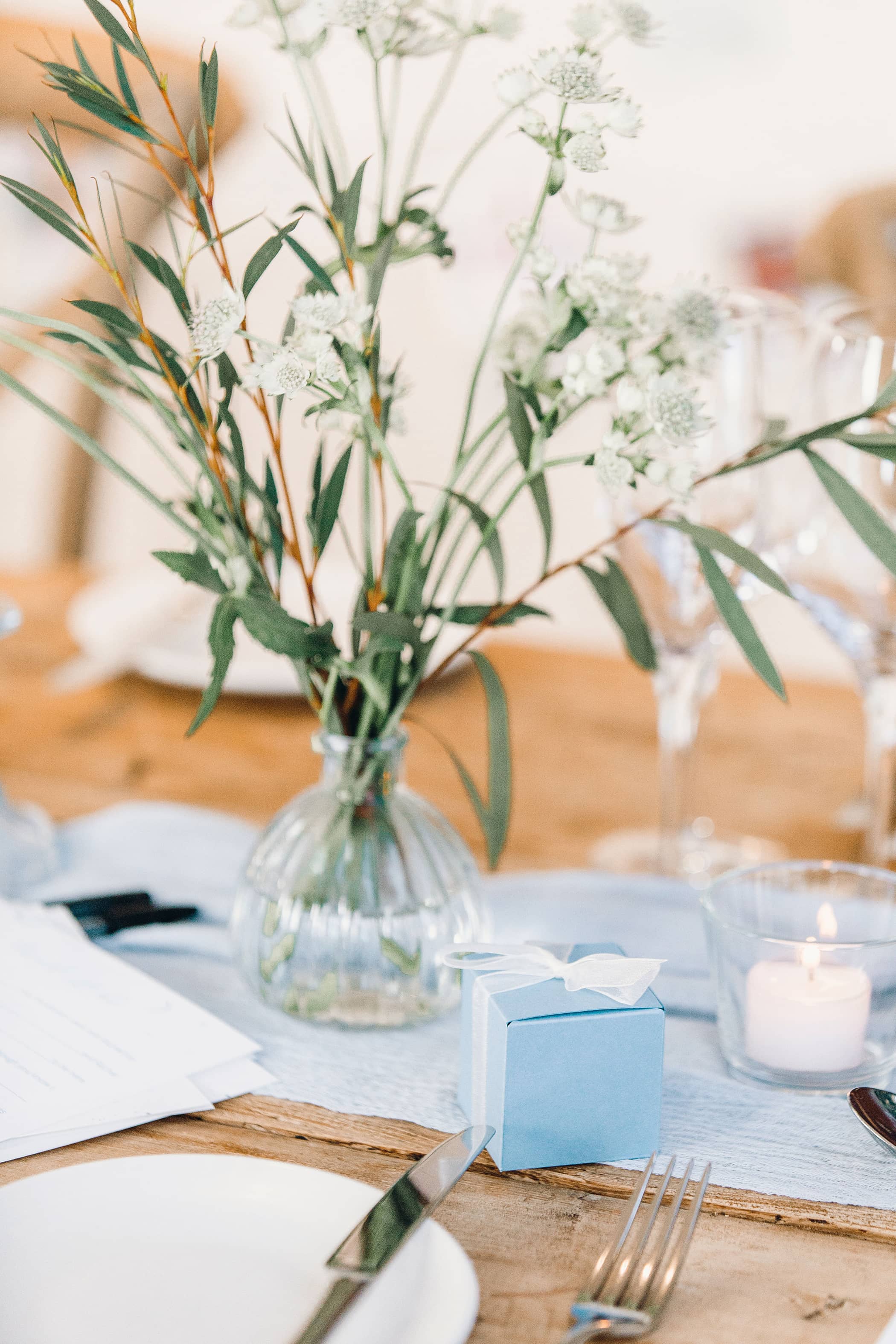 Decorative wedding table setting with pastel blue favour boxes and small bud vases containing white and blue flowers in a softly lit room at The Fig House, Middleton Lodge.