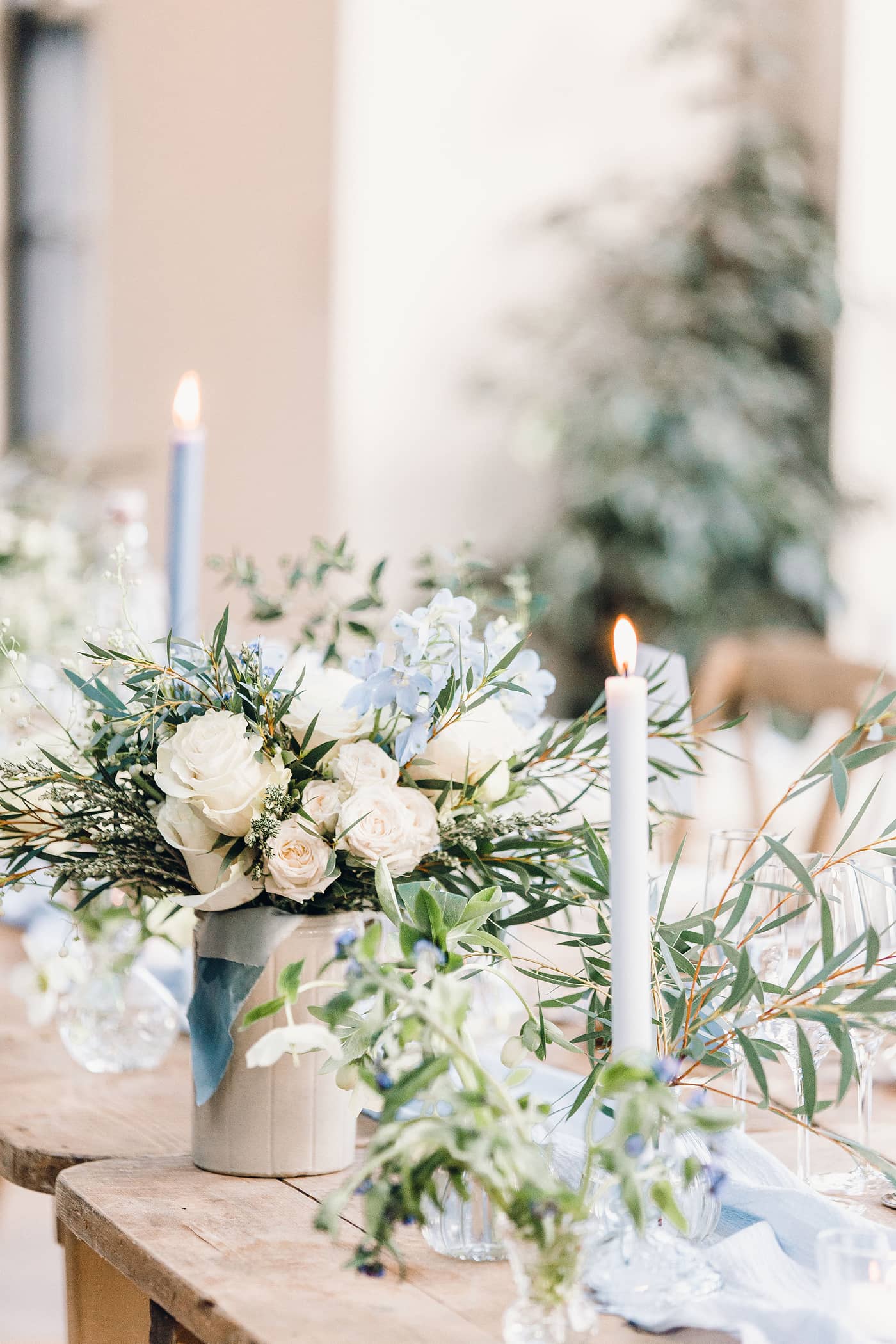 Decorative wedding table setting with white and blue floral arrangements and blue dinner candles in a softly lit room at The Fig House, Middleton Lodge.