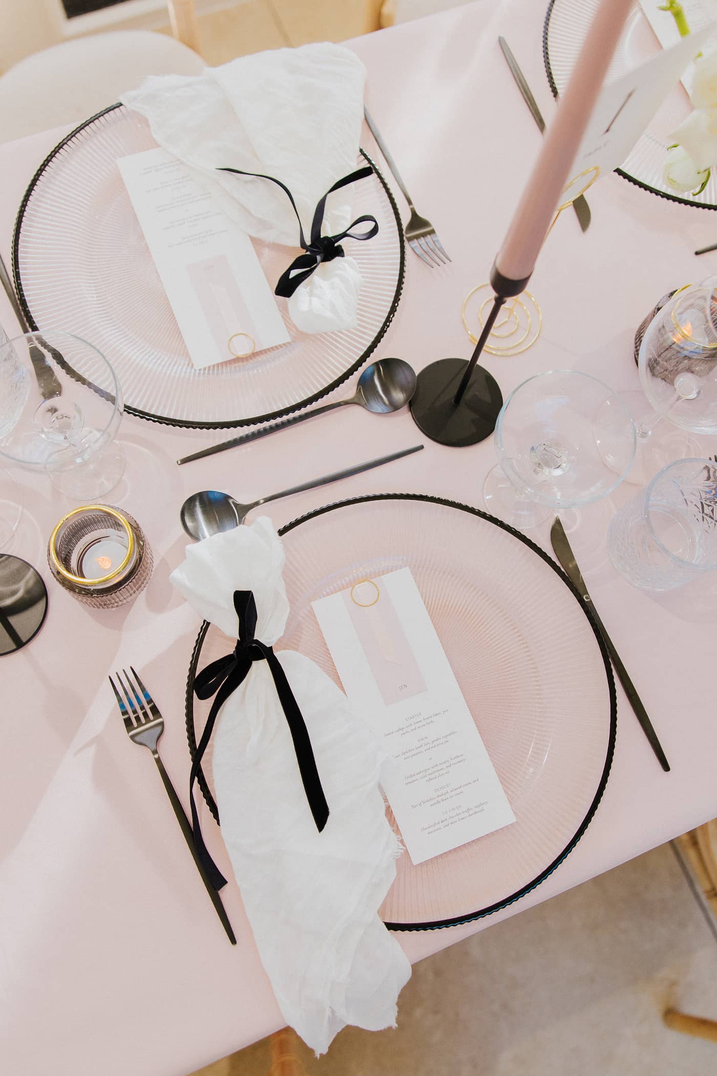 A top down view of a wedding table with pastel pink tablecloths, black cutlery and candle sticks, pink candles and a white and blush floral arrangement at Saltmarshe Hall.