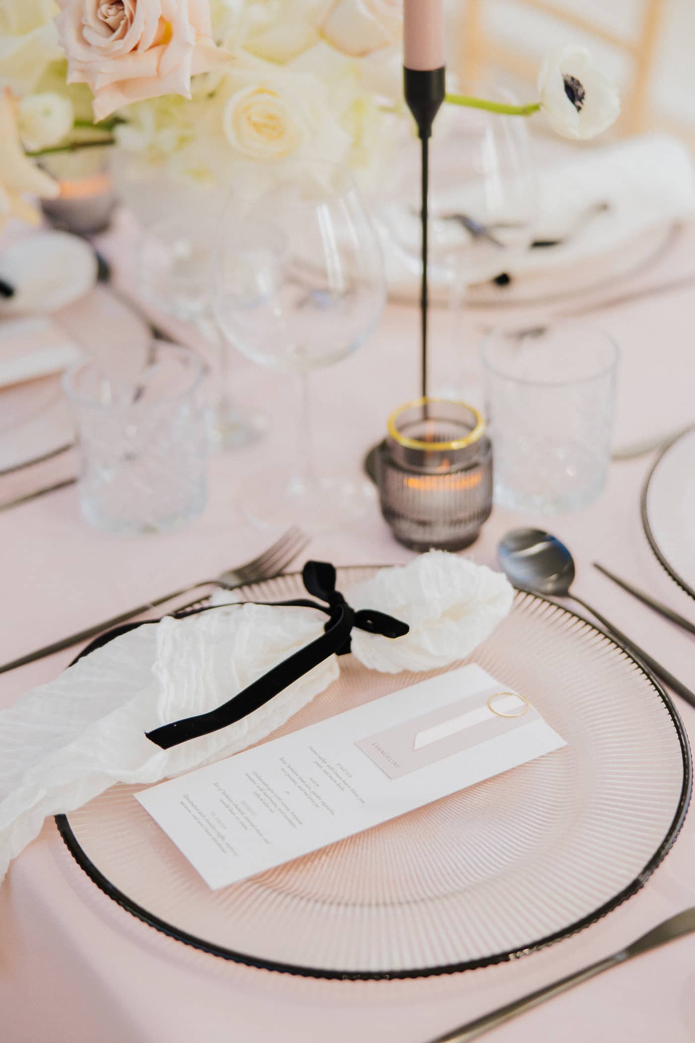 A close up of a wedding table with pastel pink tablecloths, black cutlery and candle sticks, pink candles and a white and blush floral arrangement at Saltmarshe Hall.