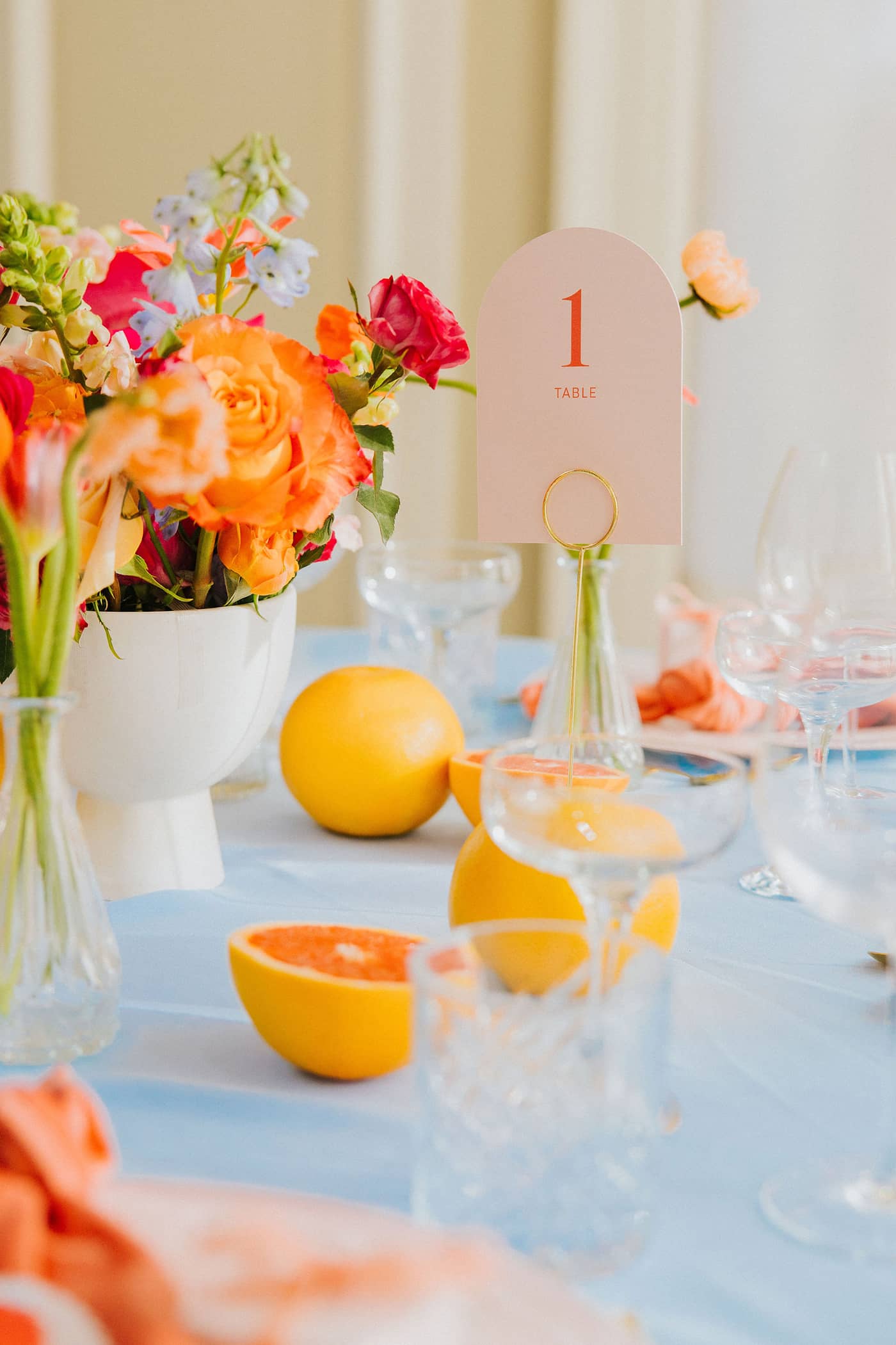 Table setting with bright orange and pastel blue flowers, lemons, and a table number on a light blue tablecloth at Saltmarshe Hall wedding venue.