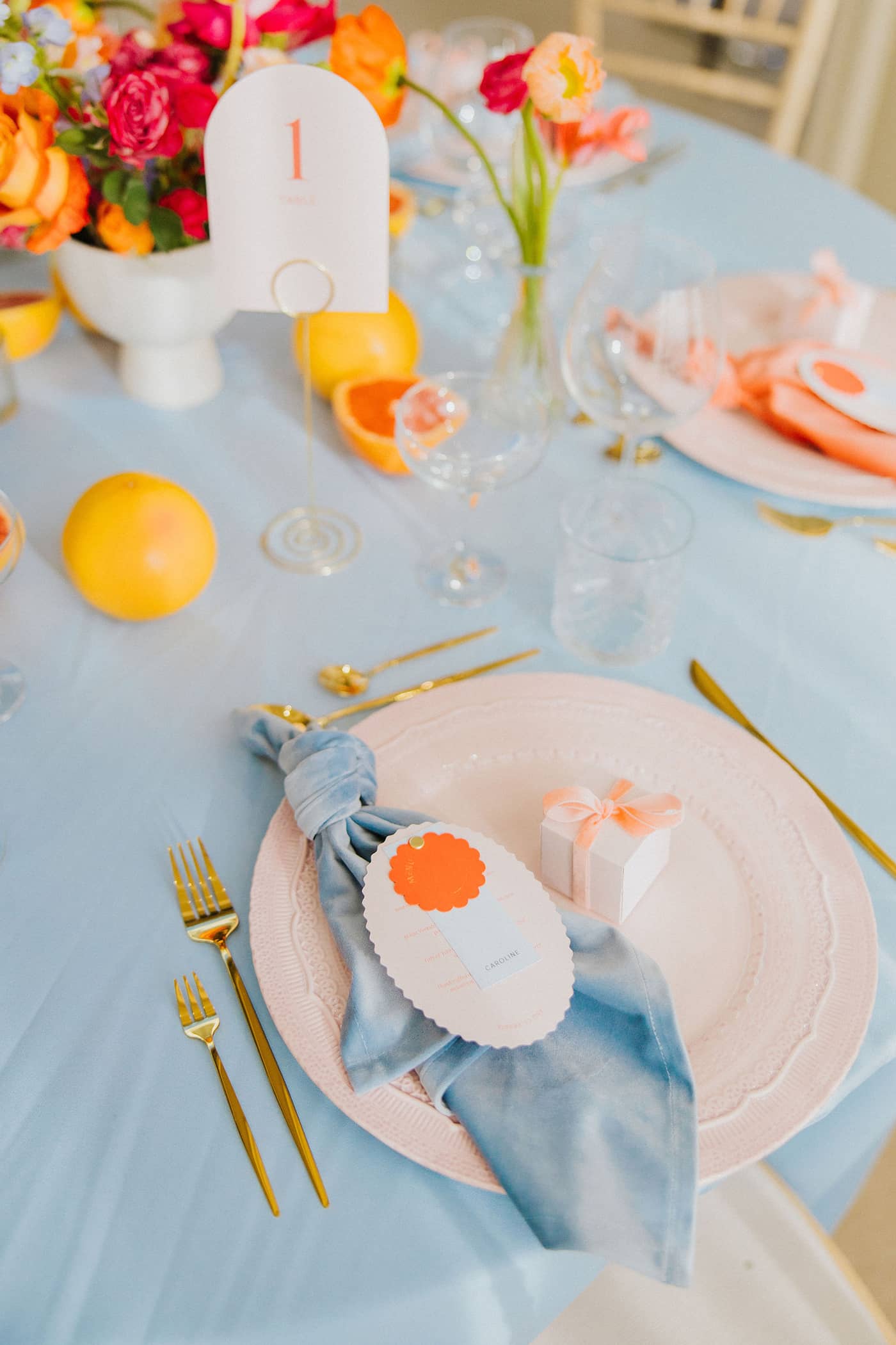 A wedding table setting with pastel pink charger plates, pastel pink favour boxes with a coral velvet ribbon and a blue. napkin, all sitting on a pastel blue tablecloth with gold cutlery. The wedding table is at Saltmarshe Hall.