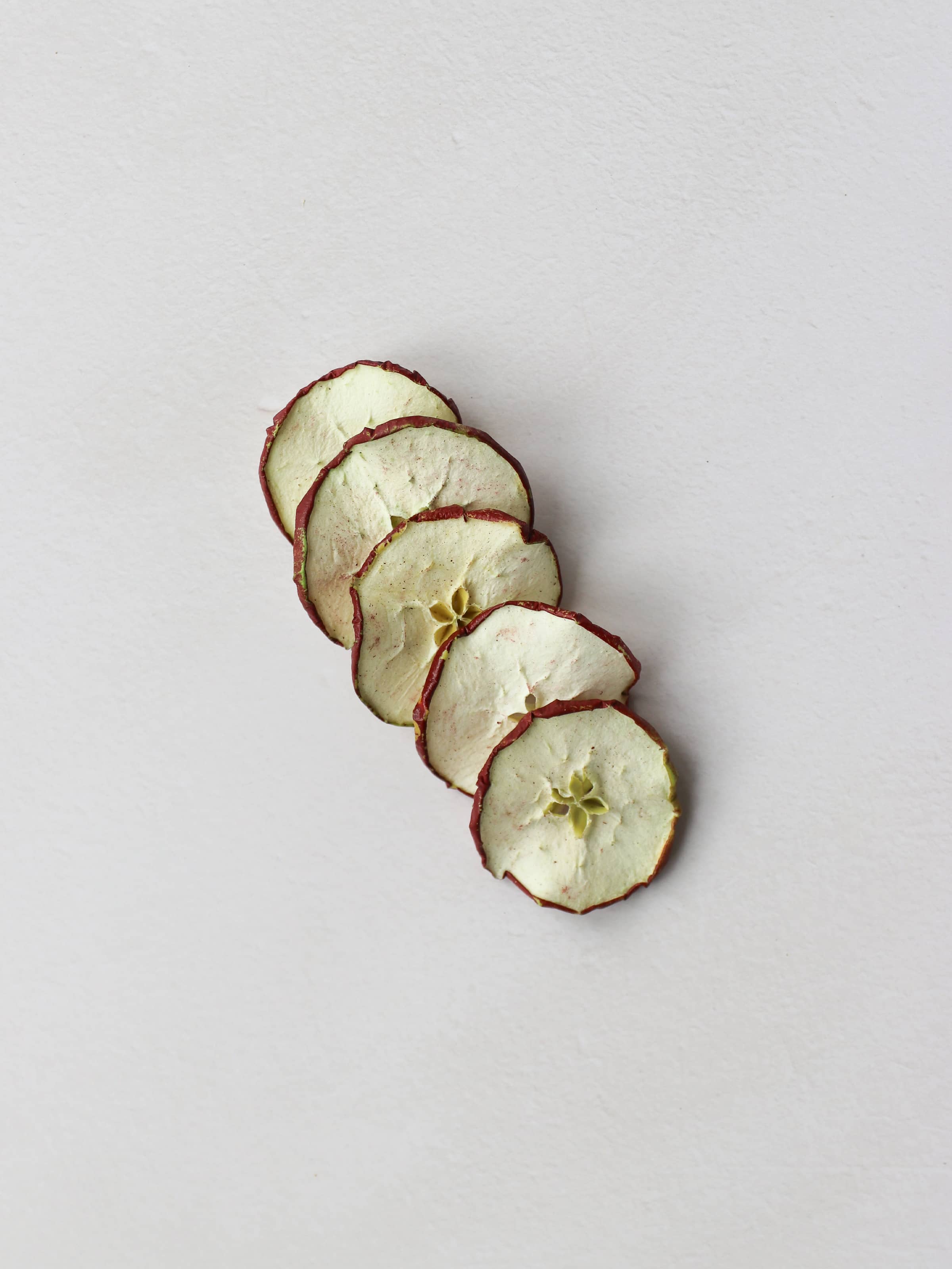 5 sliced dried red apples arranged in a row on a light background.