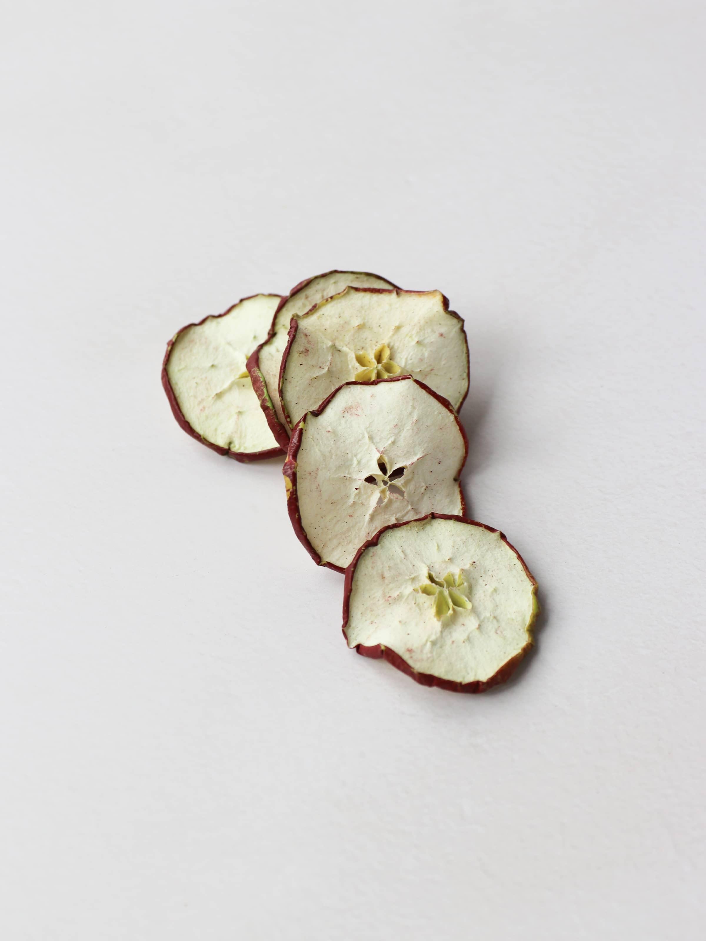 A stack of dried red apple slices for Christmas wreath making lying on a light background.