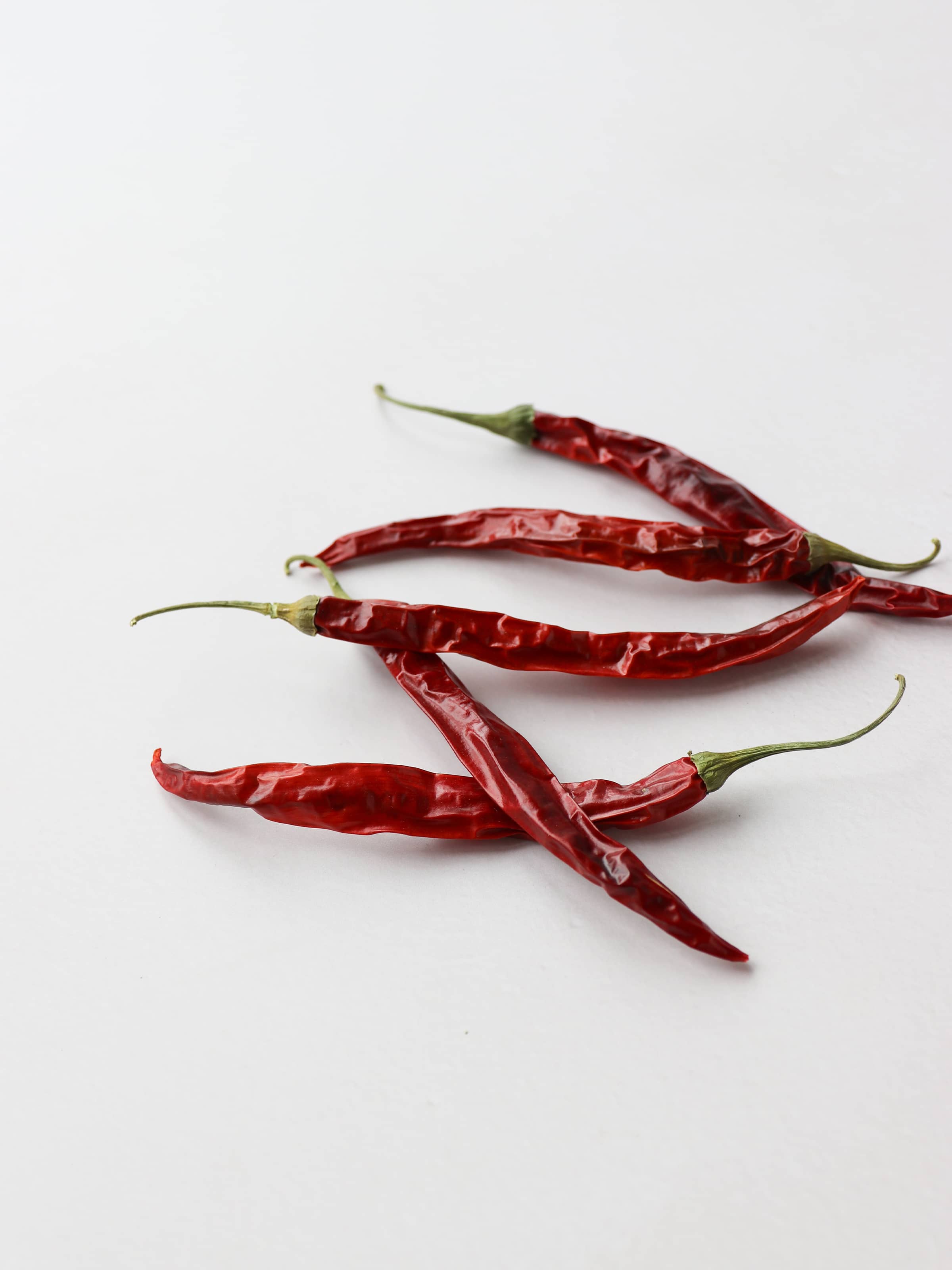 5 dried red chillies for Christmas wreath making, laying on a light background.