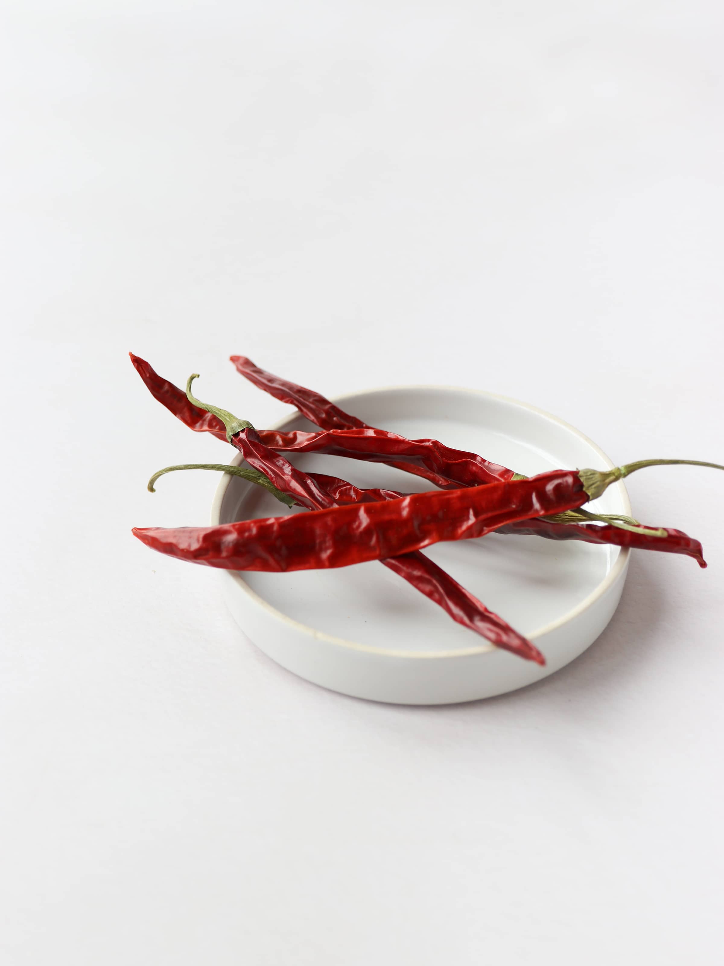 5 dried red chillies for Christmas wreath making, positioned in a white decorative bowl, on a light background.