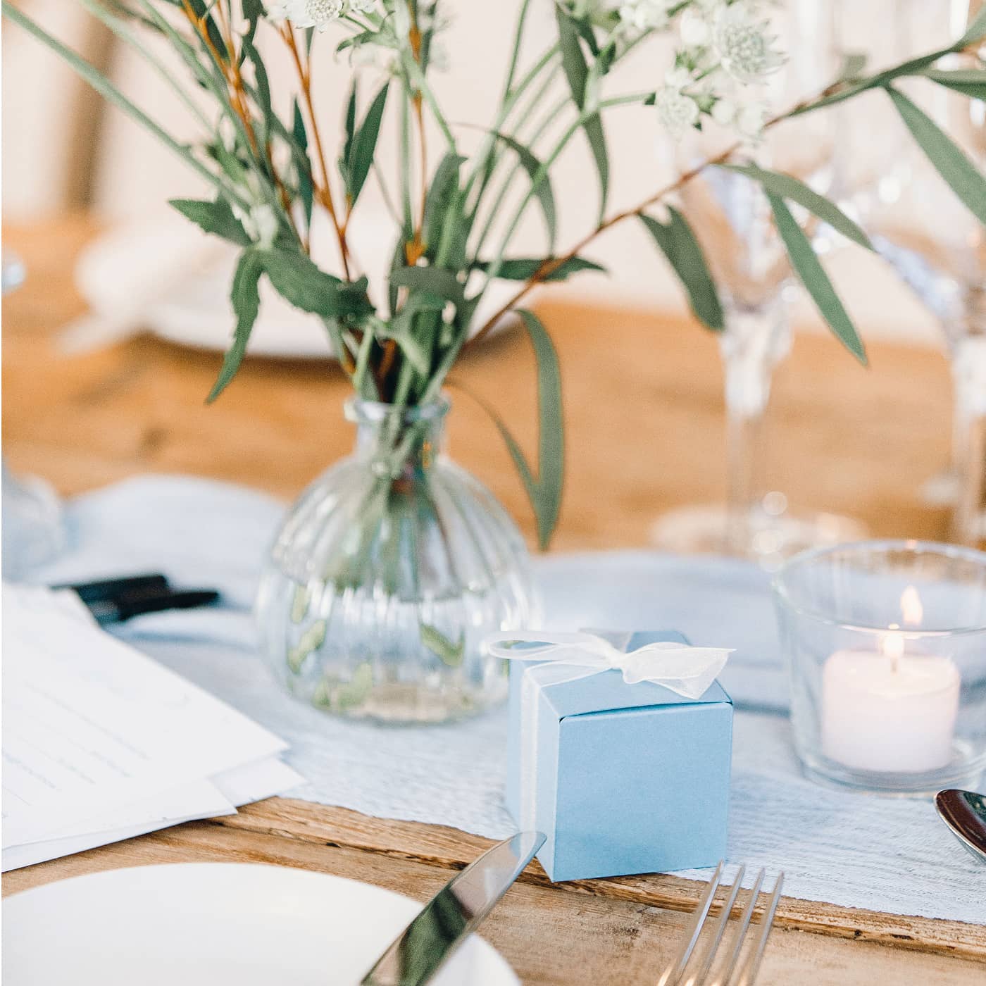 Decorative wedding table setting with pastel blue favour boxes and small bud vases containing white and blue flowers in a softly lit room at The Fig House, Middleton Lodge.