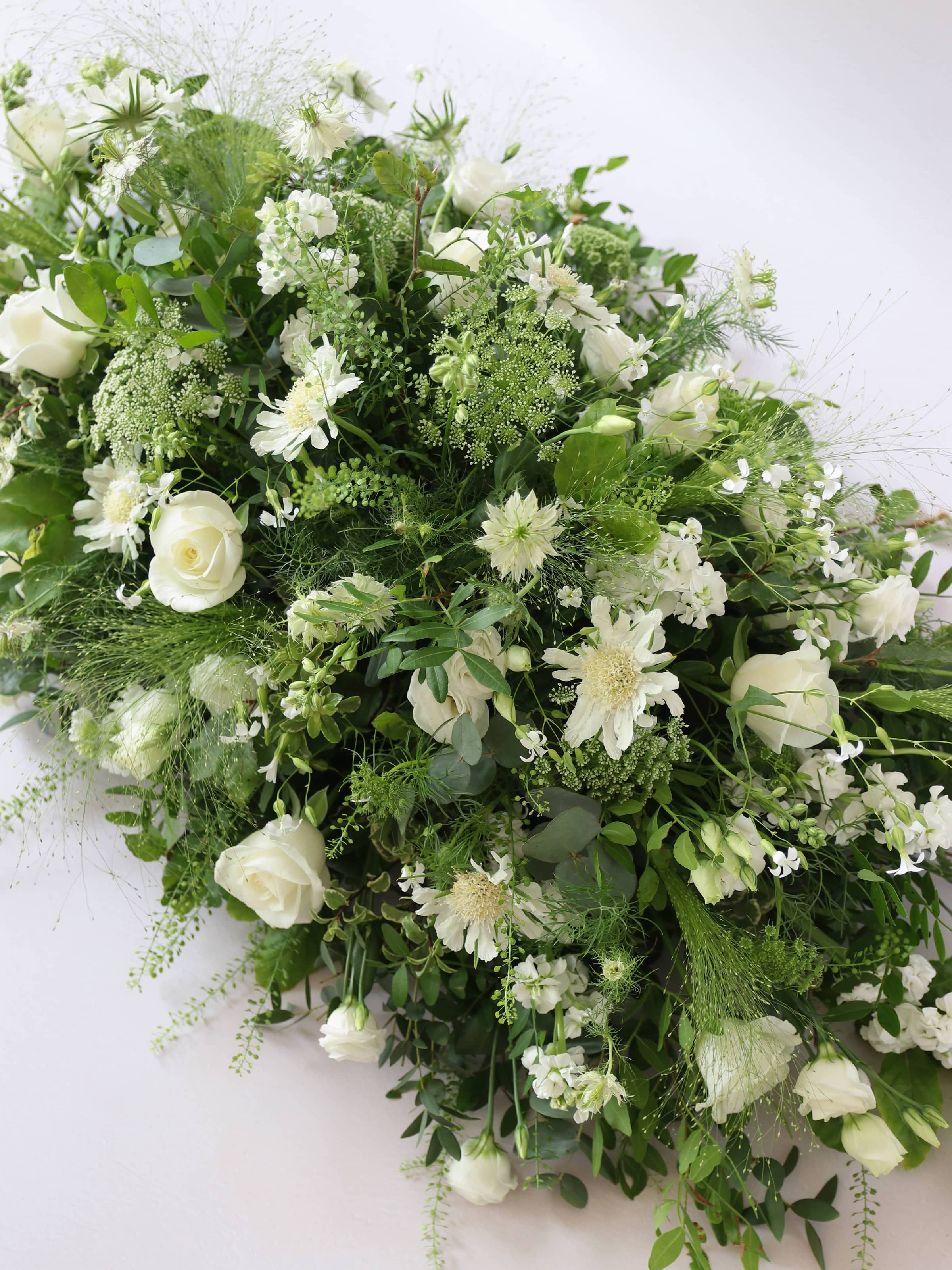 A top view of a 3ft coffin spray featuring white and green flowers and foliage. The funeral arrangement is sitting against a neutral background and features white Roses, Ammi, Stocks and Lisianthus.
