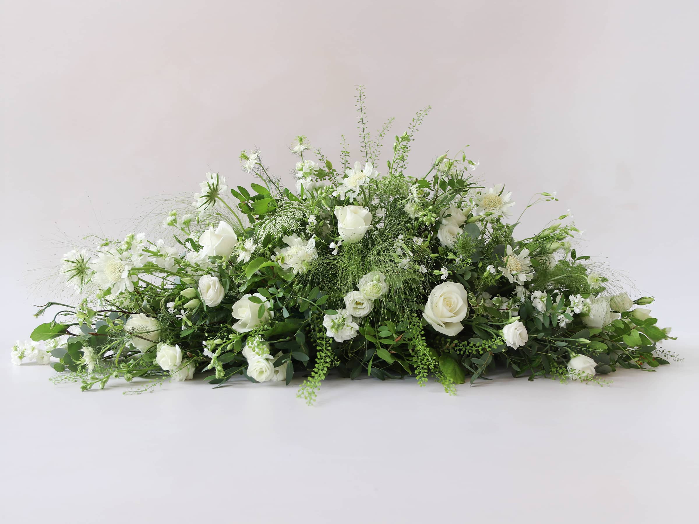 A side view of a 3ft coffin spray featuring white and green flowers and foliage. The funeral arrangement is sitting against a neutral background.