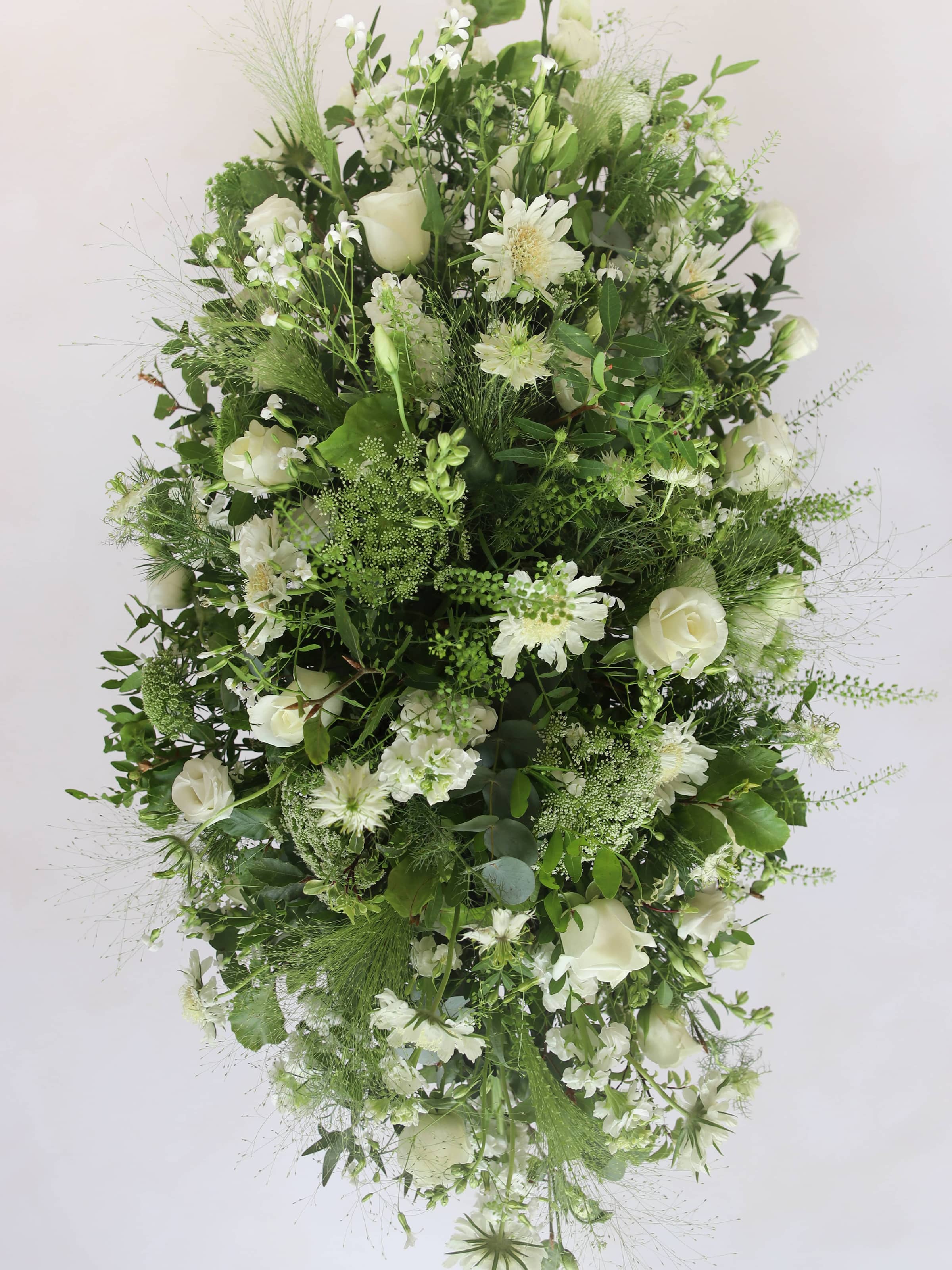 A top view of a 3ft coffin spray featuring white and green flowers and foliage. The funeral arrangement is sitting against a neutral background and features white Roses, Ammi, Stocks and Lisianthus.