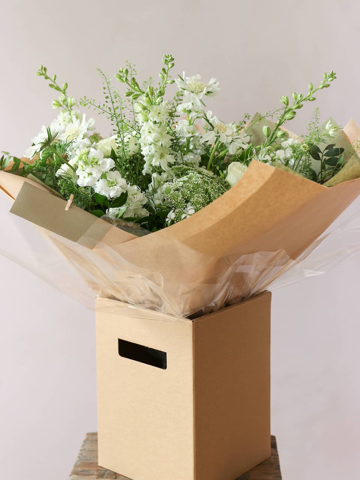 White & Green floral arrangement in an aqua pack within a  cardboard box on a light background