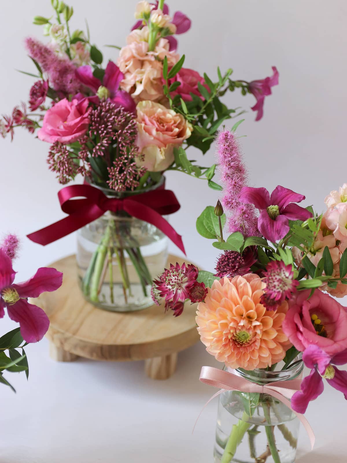 Three small floral arrangements in glass jars with pink and purple flowers on a white background
