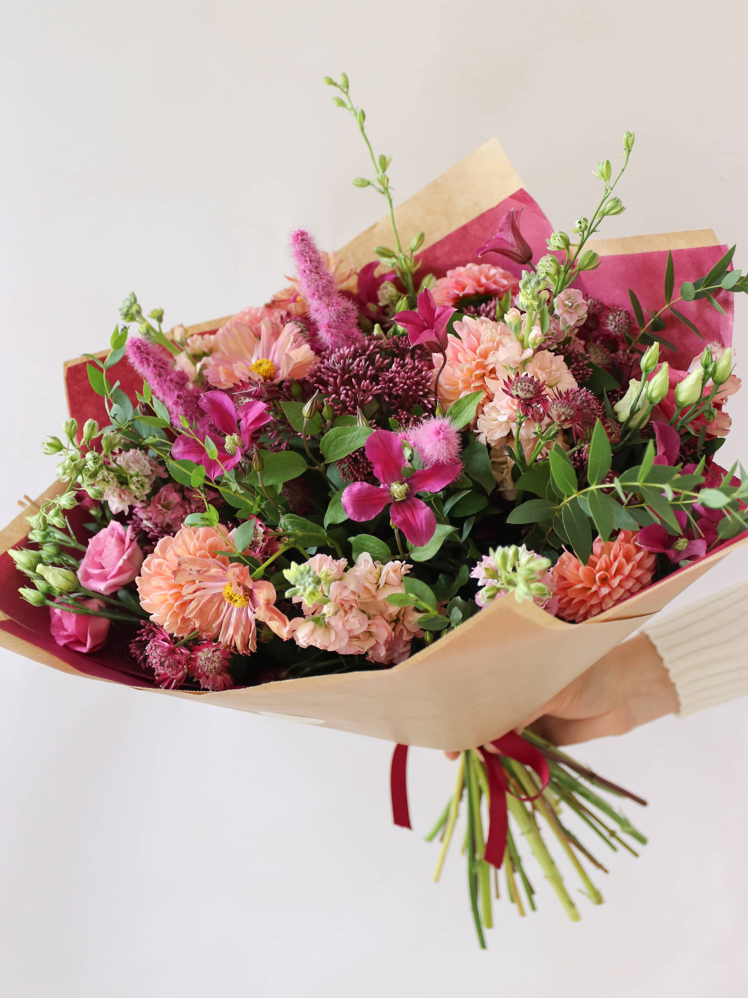 Bouquet of bright pink and peach flowers wrapped in brown paper with a white background