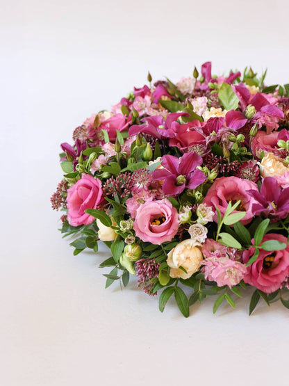 Off canvas view of a round funeral posy of bright pink and peach flowers with green foliage on a white background