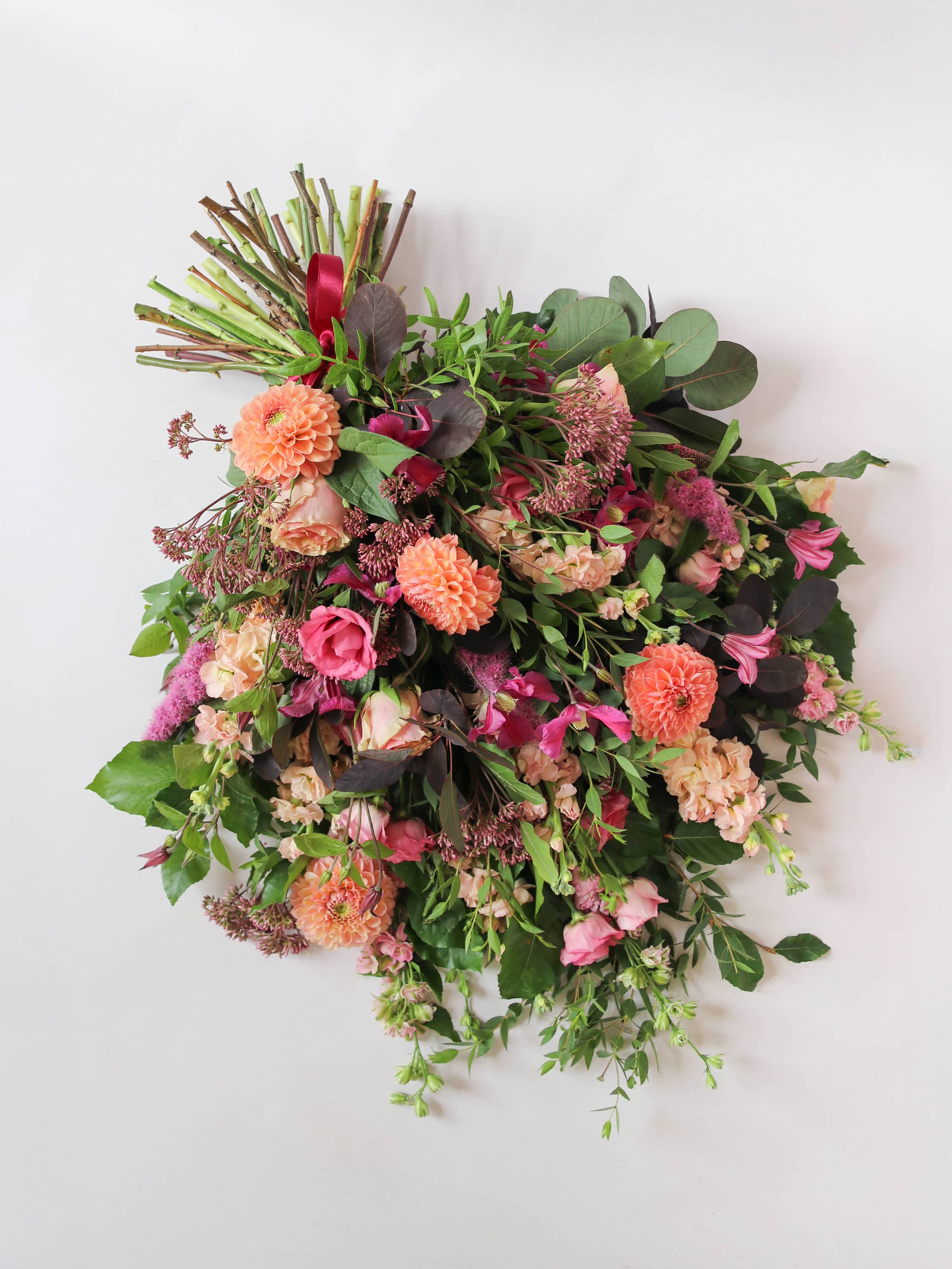 Top down view of a funeral sheaf with bright pink and peach flowers with green foliage on a white background