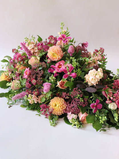 Bright pink and peach coffin spray with green foliage at an angle on a white background