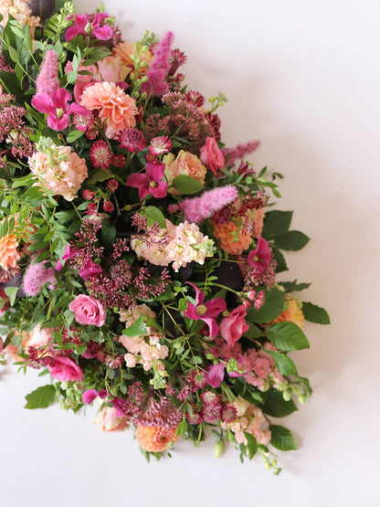 One end of a double ended coffin spray with bright pink and peach flowers, on a white background