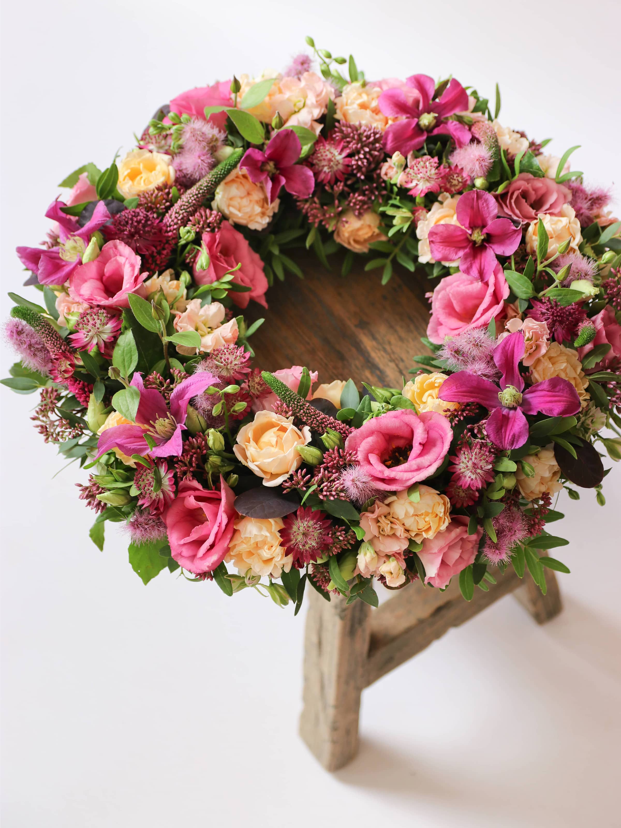 Floral wreath with pink and yellow flowers on a white background atop a wooden stool.