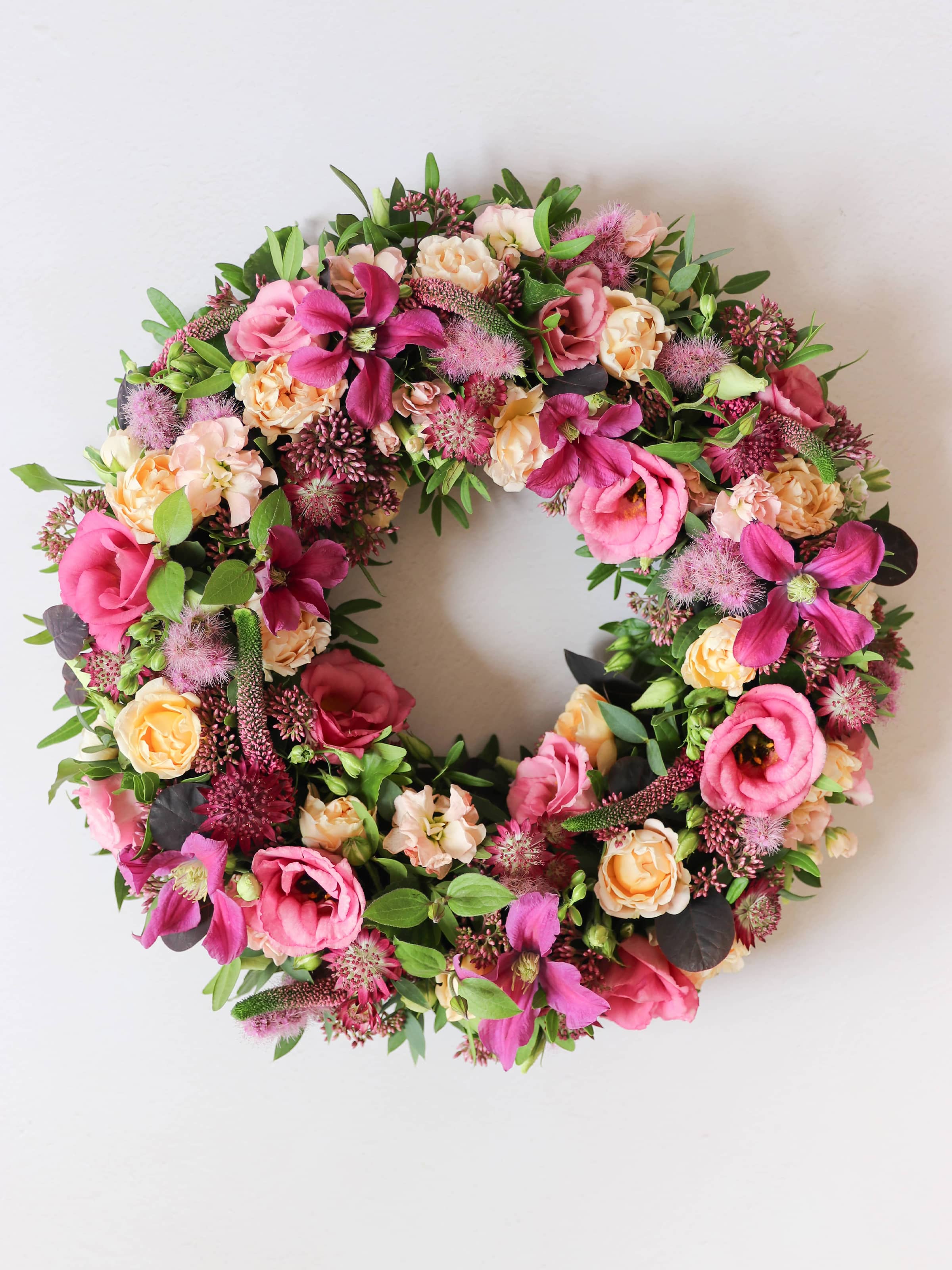 Top down view of a floral wreath with pink, yellow, and green flowers on a white background