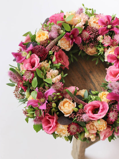 Floral wreath with pink, yellow, and green flowers on a wooden stool