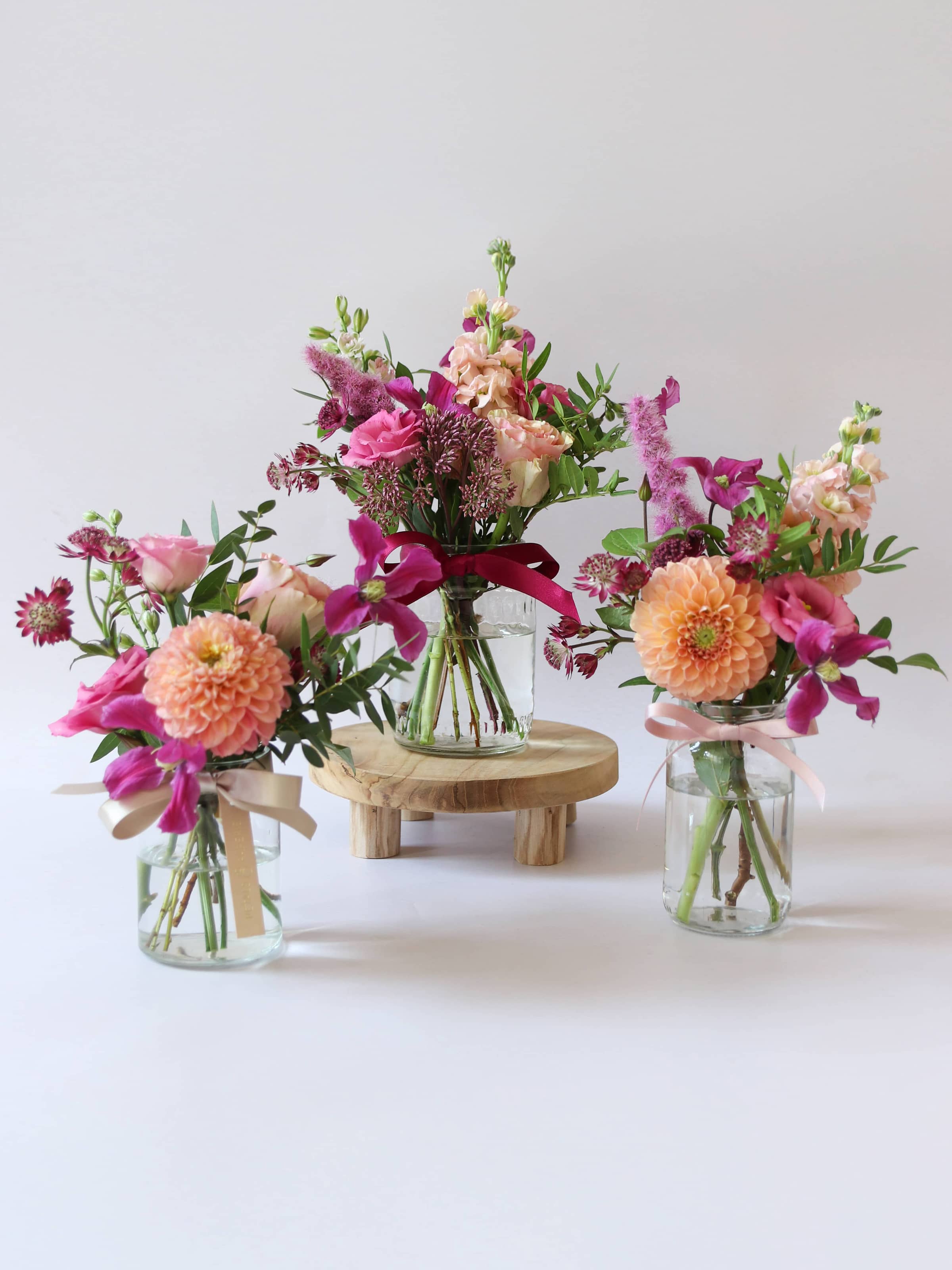 Three bright pink and peach arrangements in glass jam jars on a white background