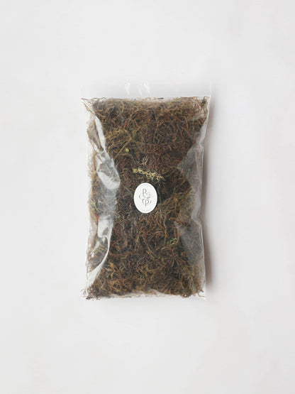 A bag of sphagnum moss packaged in an air-tight plastic resealable bag. The bag has a branded Petals & Paperie sticker on the front and is positioned on a neutral background.