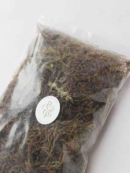 A bag of sphagnum moss packaged in an air-tight plastic resealable bag. The bag has a branded Petals & Paperie sticker on the front.